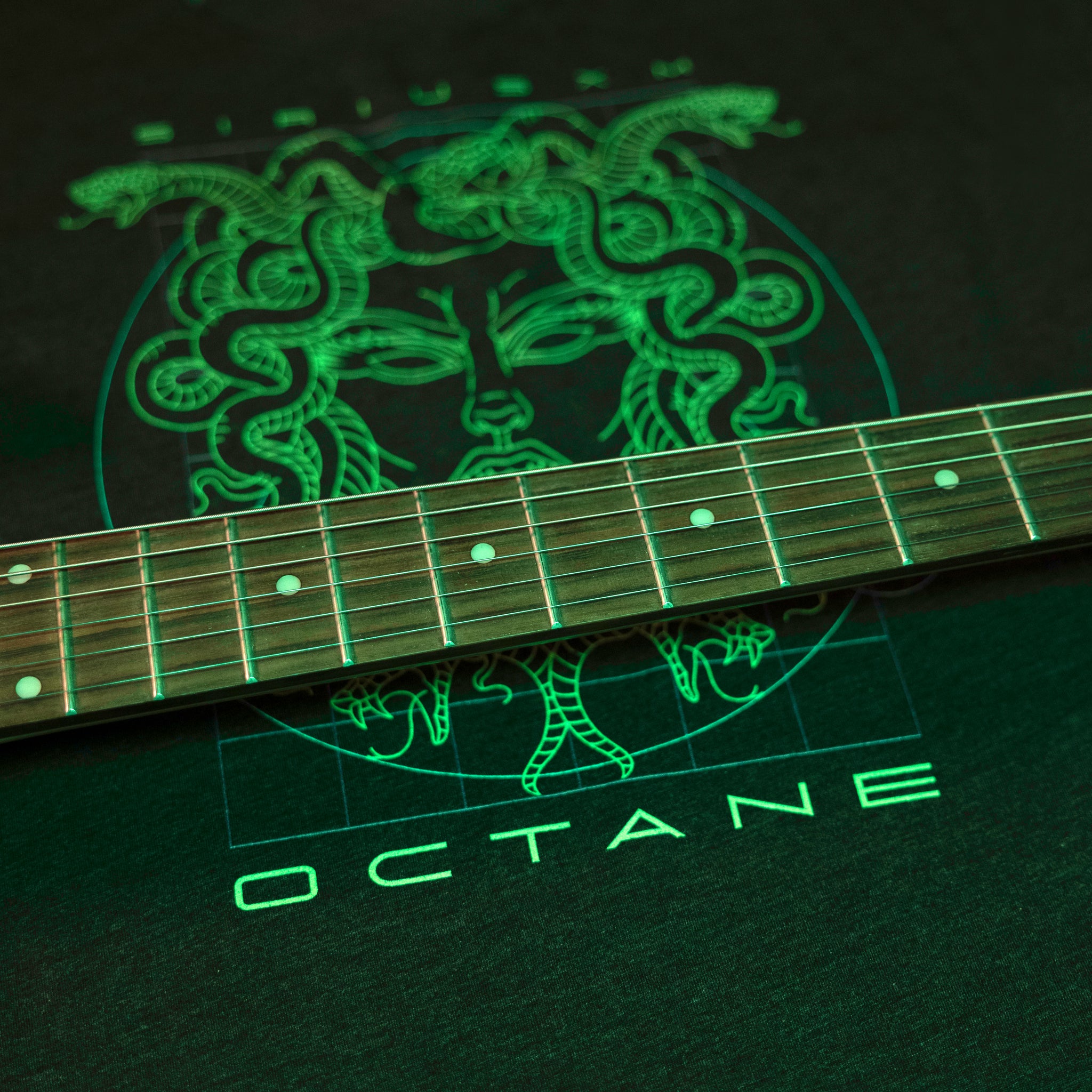 A guitar rests on a black T-shirt featuring a glowing Medusa design with the word 'OCTANE.'