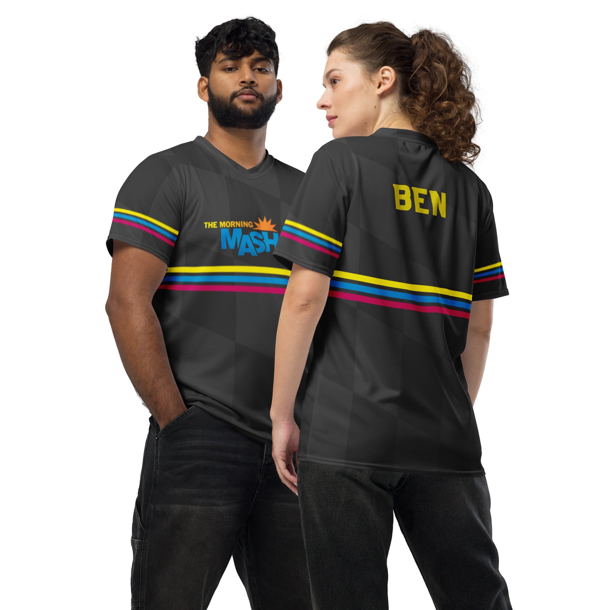 Two models, a man and a woman, stand against a white background.  They wear matching black sports jerseys with colorful horizontal stripes on the sleeves and back. The front of the man's jersey features the partially visible 'THE MORNING MASH UP' logo, while the back of the woman’s jersey has the name 'BEN' printed in gold lettering. The models stand in relaxed poses, with the woman slightly turned to showcase the back of the jersey while the man faces forwards with a hand in his pocket.