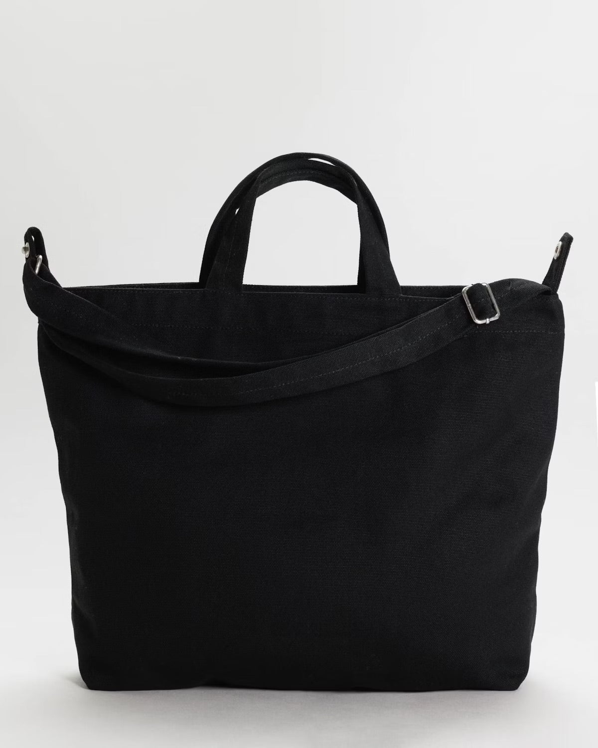 Back of a  black tote bag with two short handles and a longer shoulder strap, set against a light background.