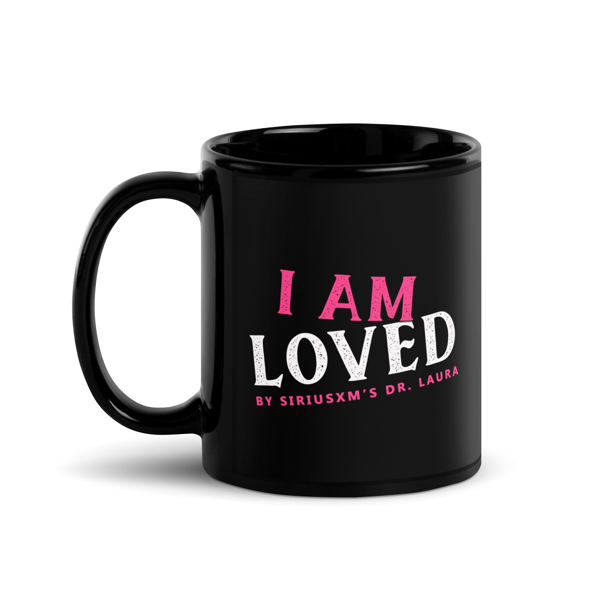 A black glossy ceramic mug with the handle on the left side. The text on the front reads 'I AM LOVED,' with 'I AM' in pink and 'LOVED' in white lettering. Below, it says 'BY SIRIUSXM'S DR. LAURA' in smaller pink text.