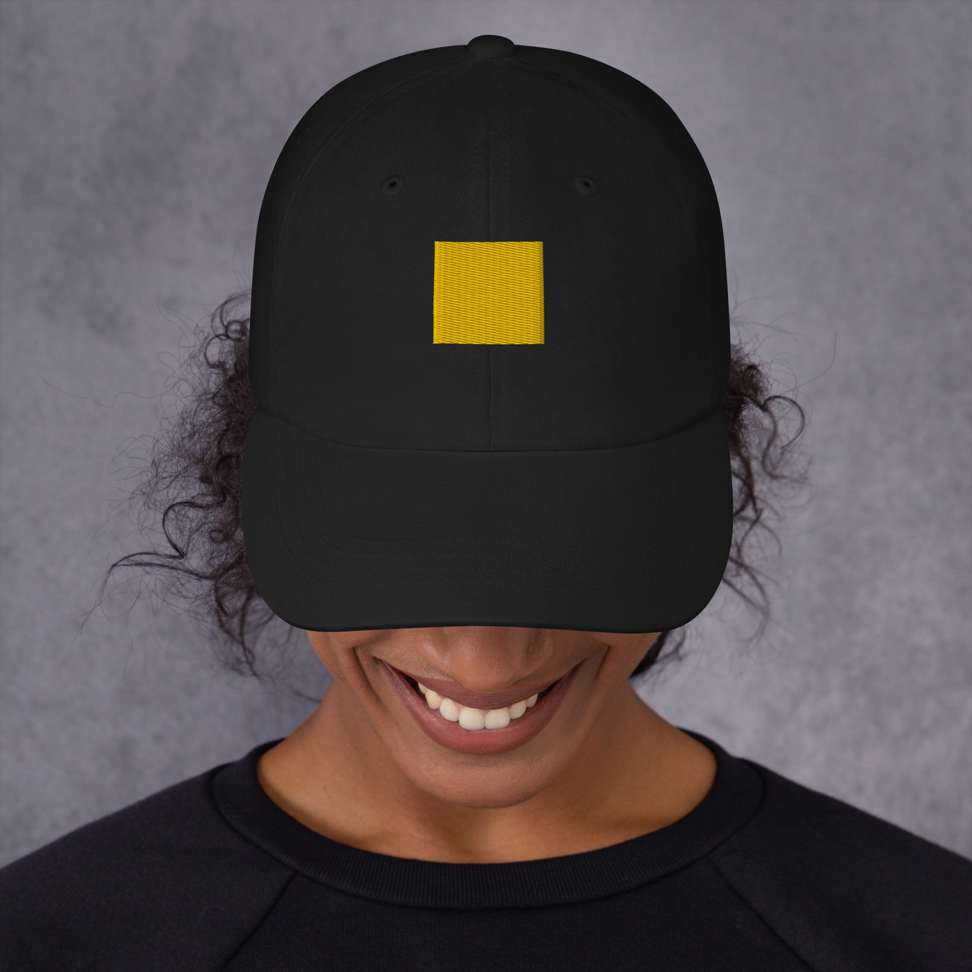 A person wearing a black cap with a yellow square on the front.