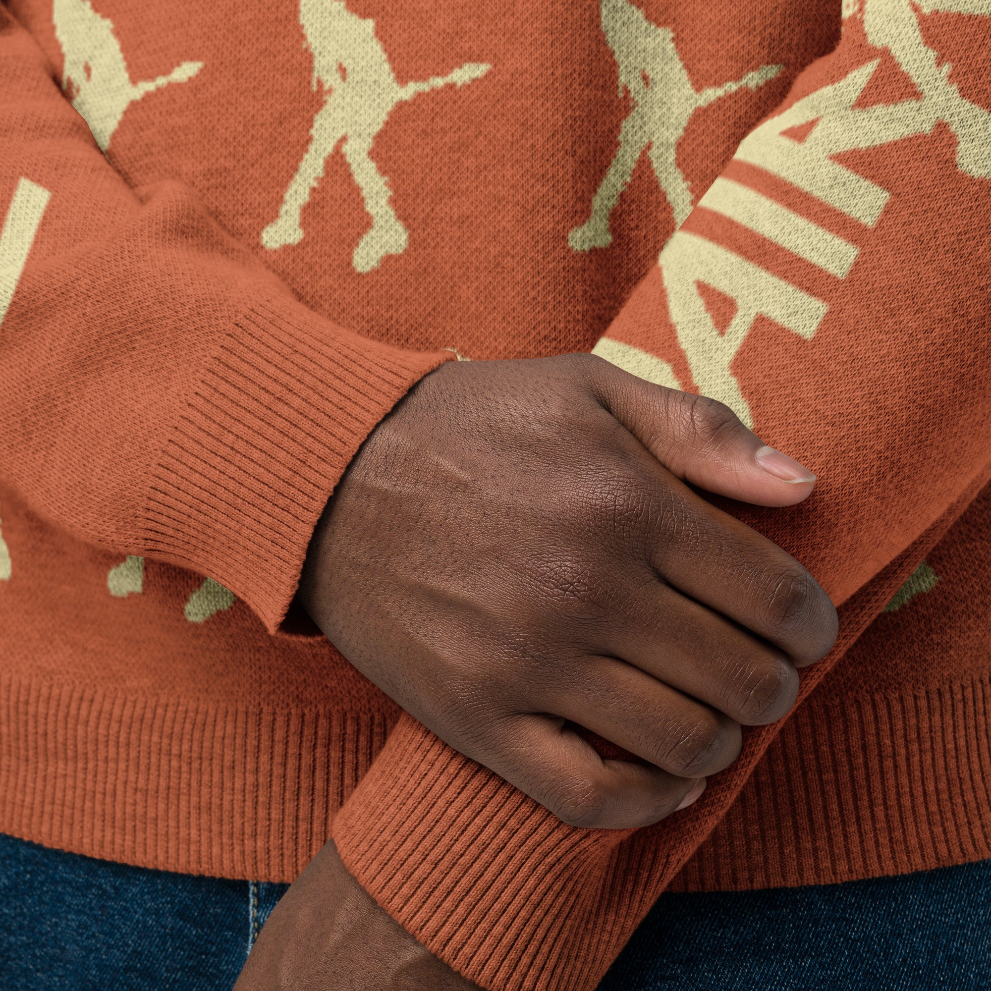 Close-up of hands wearing an orange sweater featuring a pattern of yellow silhouettes and text.