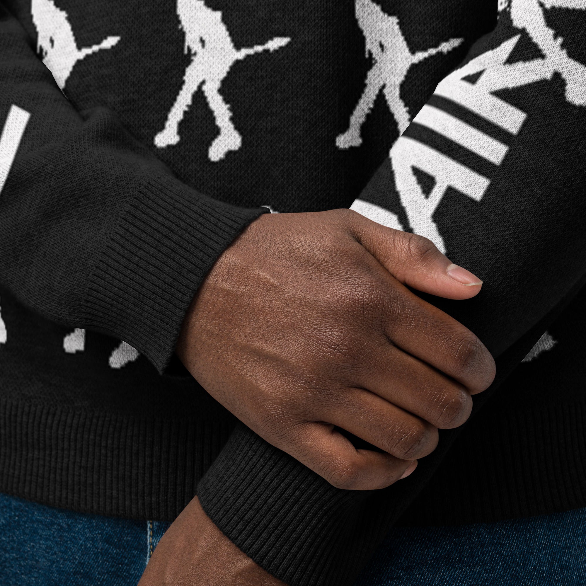 Close up of person's hands wearing a black sweater featuring a white repeating pattern of guitarists.