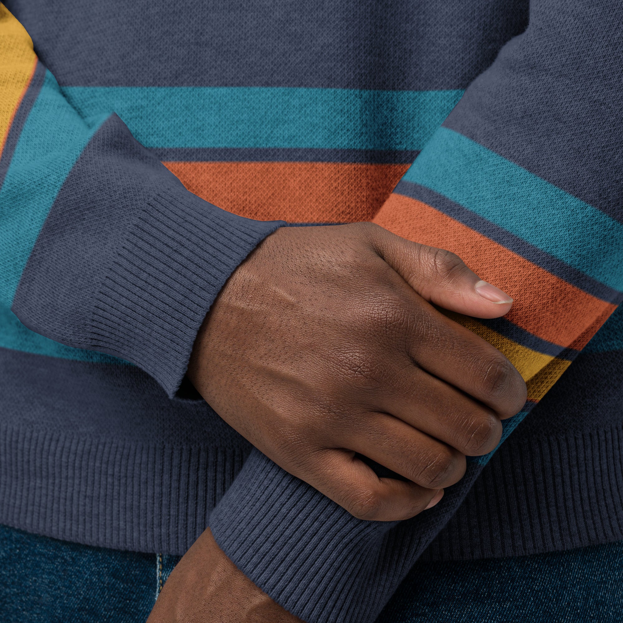 Close-up of hands wearing a navy sweater with stripes of blue, orange, yellow, and blue (repeated) above sleeves and cuffs.