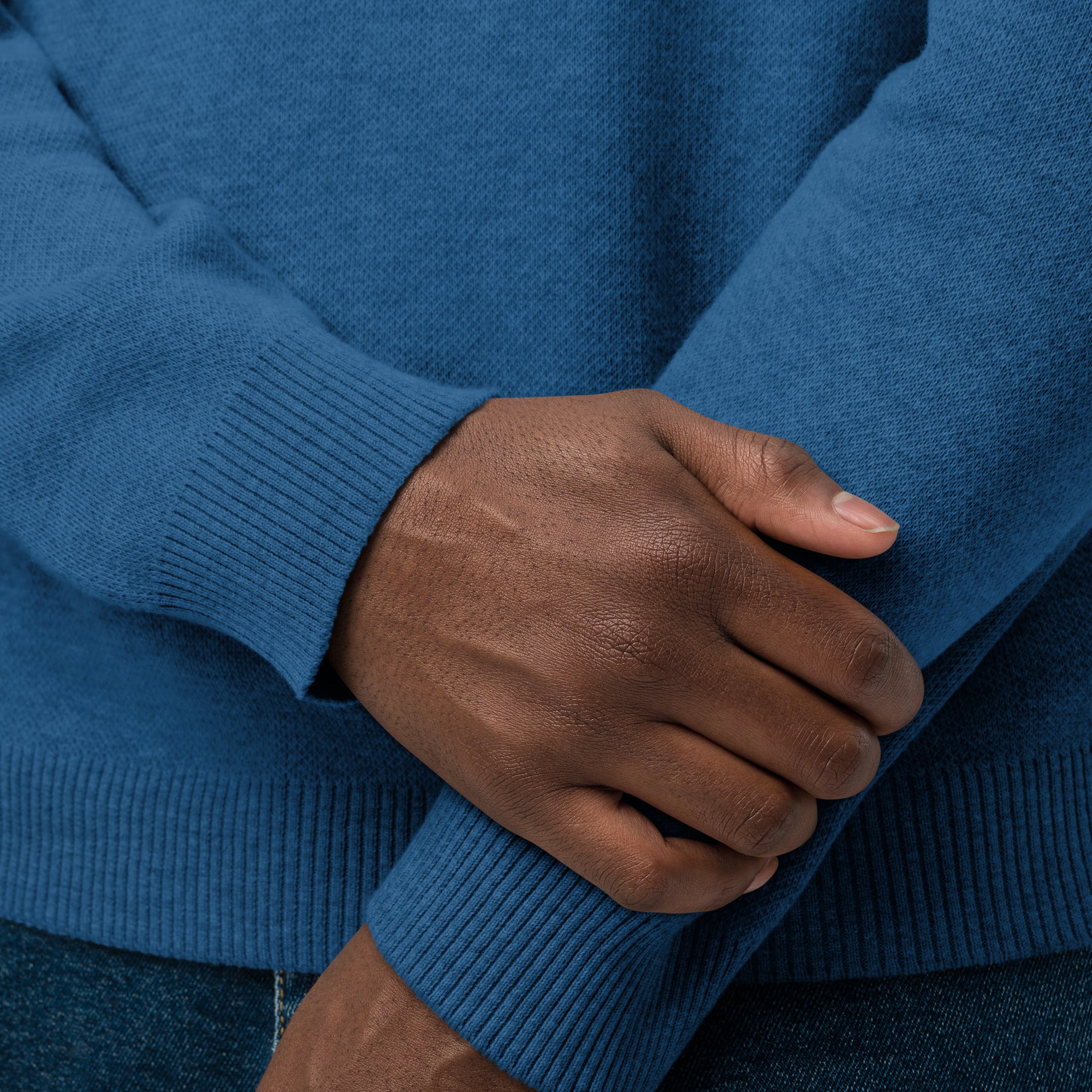 Close-up of hands wearing a blue sweater, focusing on the ribbed cuffs and arms.