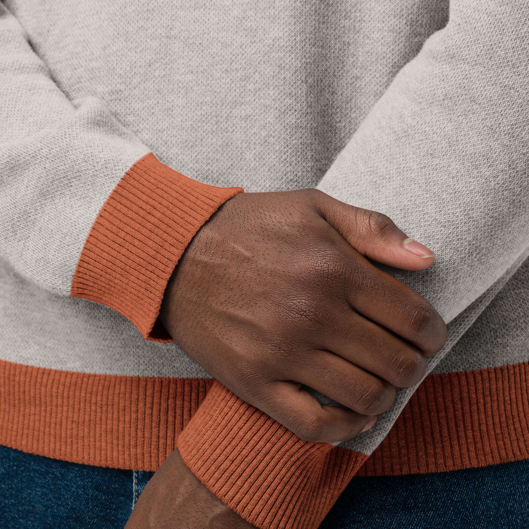 A close-up of hands wearing a sand colored sweater with orange ribbed cuffs and hem