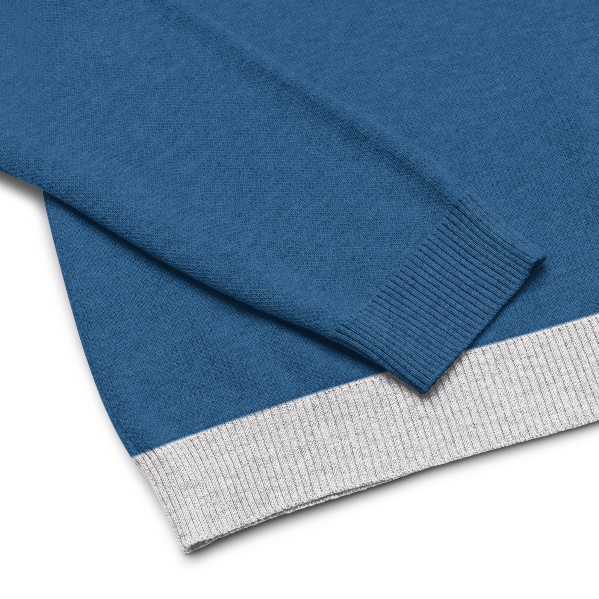 A close-up of a blue sweater showing the sleeve and hem with a light gray ribbed trim.