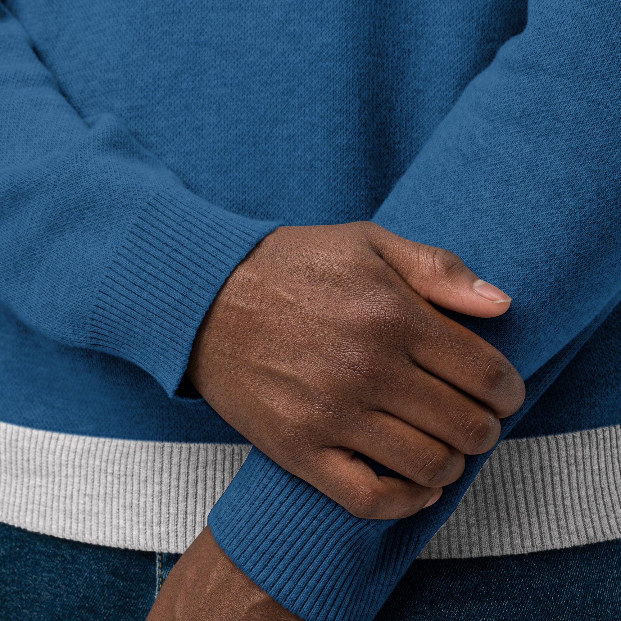 Close-up of hands wearing a blue sweater with ribbed cuffs and a light gray band at the bottom.