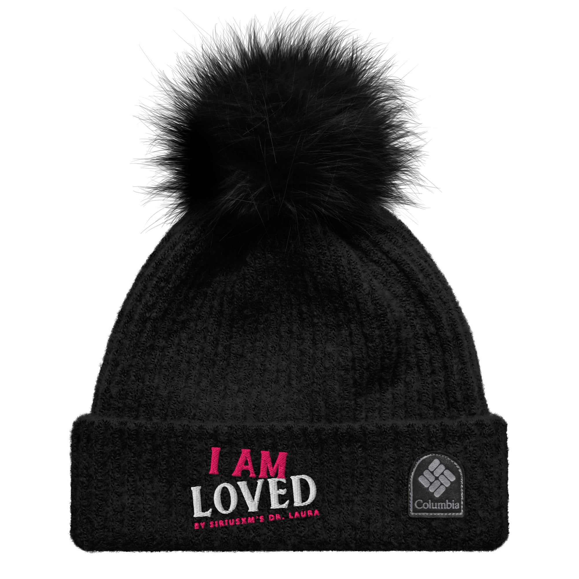 Black, ribbed beanie hat with matching, fluffy pom-pom on top laying flat on a white background. Folded cuff features embroidered wording 'I AM LOVED,' with 'I AM' in pink and 'LOVED' in white lettering. Below, it says 'BY SIRIUSXM'S DR. LAURA' in smaller pink text and 'Columbia' branded patch. 