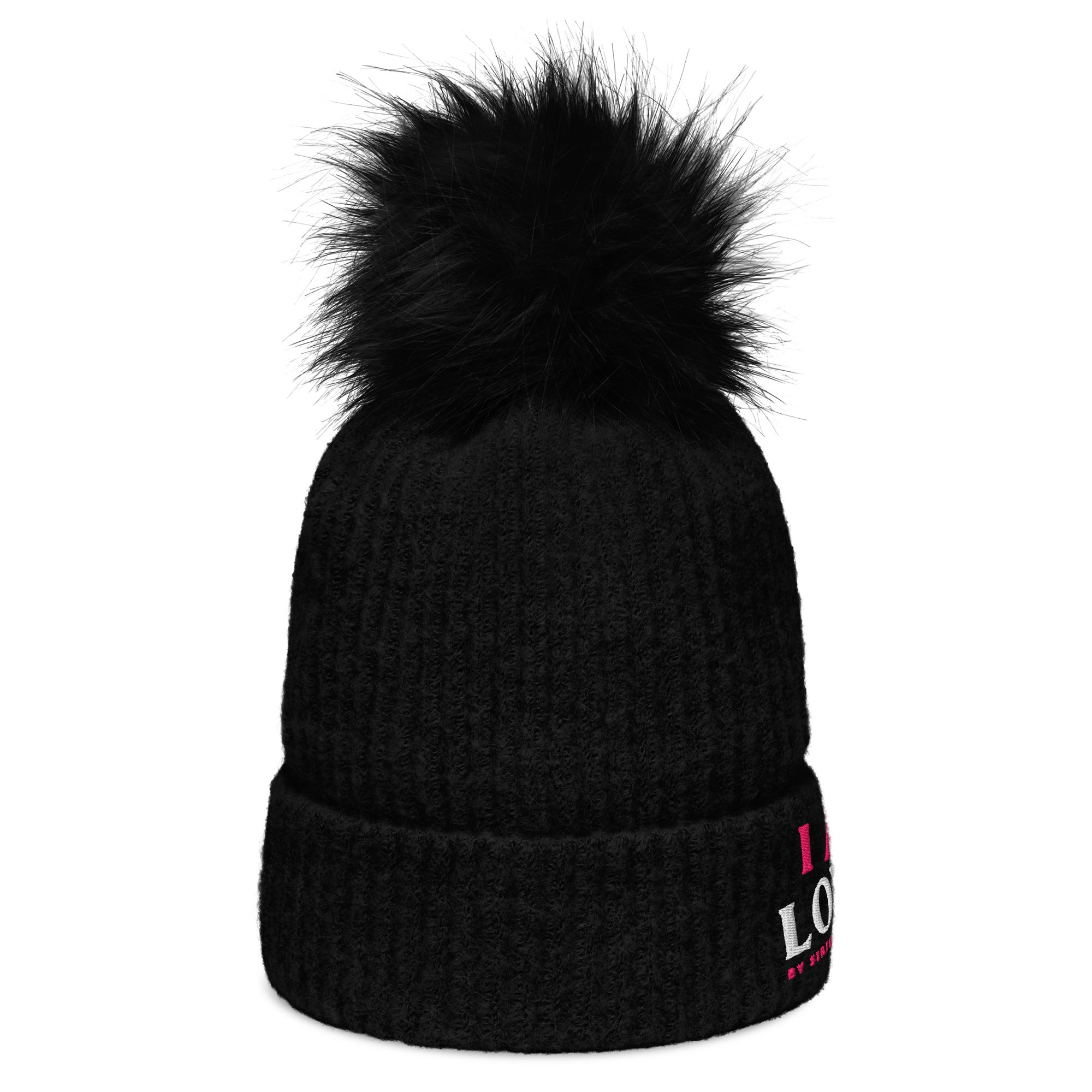 Side view of a black knit beanie with a fluffy black pom-pom on top. Partially visible front side logo featuring pink and white lettering, along with a folded cuff for added style.