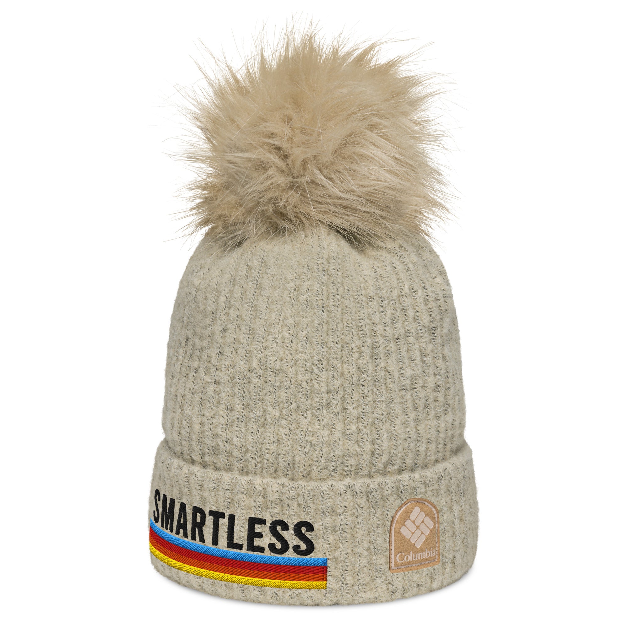 A cream-colored knit pom-pom beanie with 'SMARTLESS' embroidered on the front, accompanied by a rainbow stripe design. The beanie also features a 'Columbia' logo patch on the cuff.