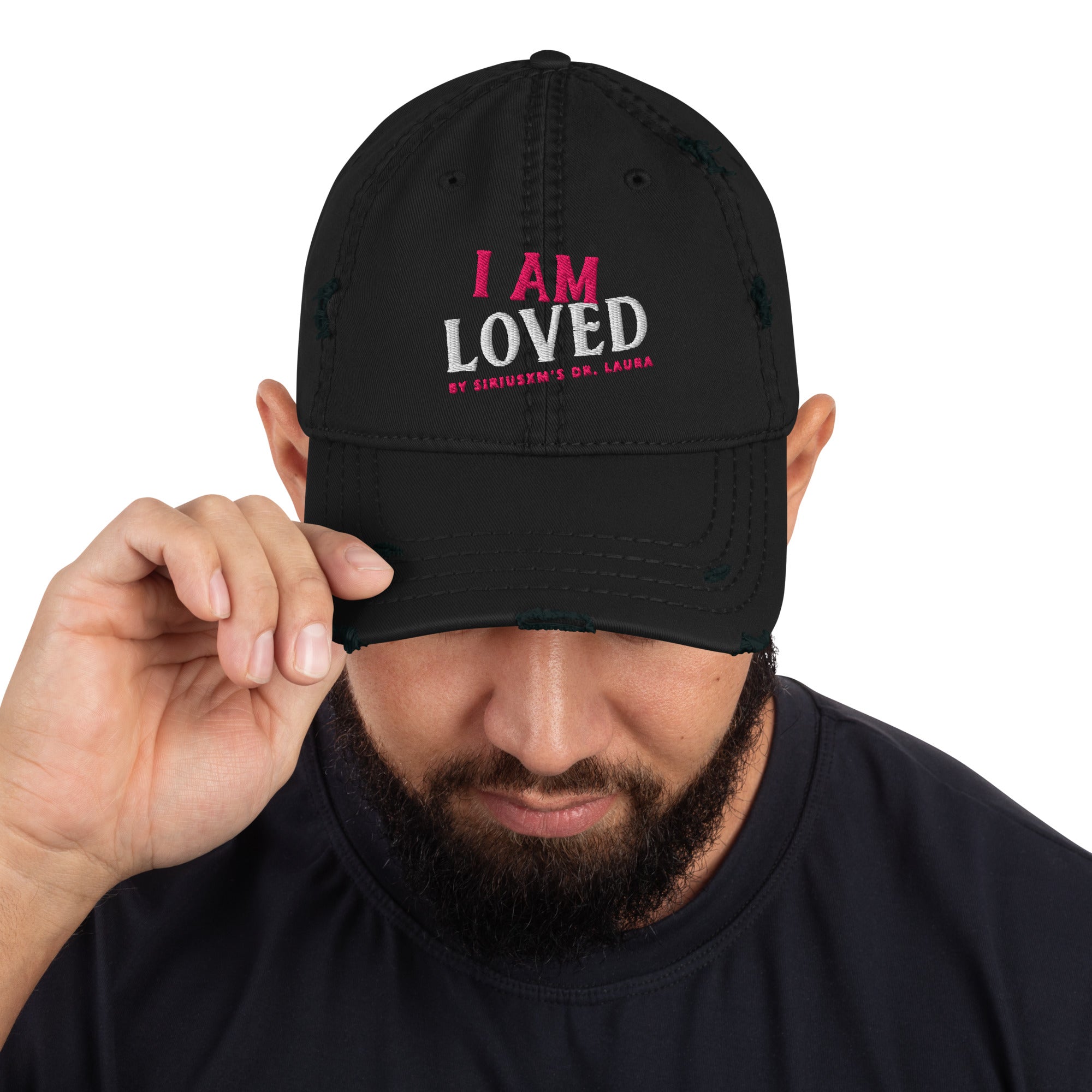 A bearded man wearing a black dad-style baseball cap, holding the left side of the brim. The text reads 'I AM LOVED,' with 'I AM' in pink and 'LOVED' in white textured lettering. Below, it says 'BY SIRIUSXM'S DR. LAURA' in smaller pink text.