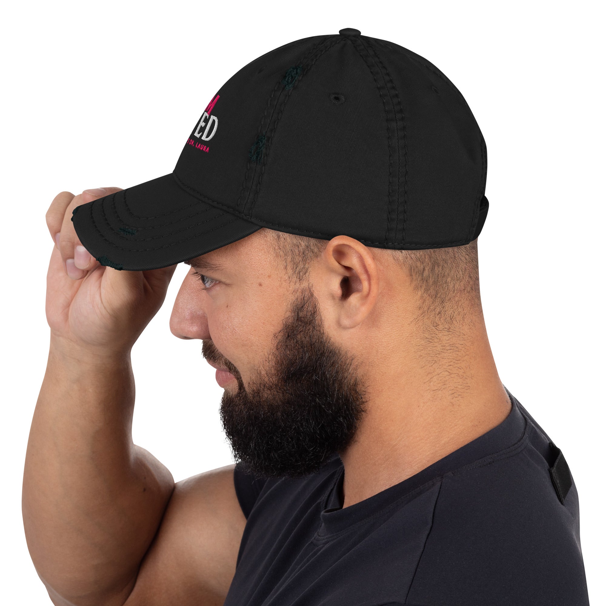 Profile of a bearded man facing left, holding the brim of a black baseball hat, featuring partial view of front side graphic's pink and white lettering. 