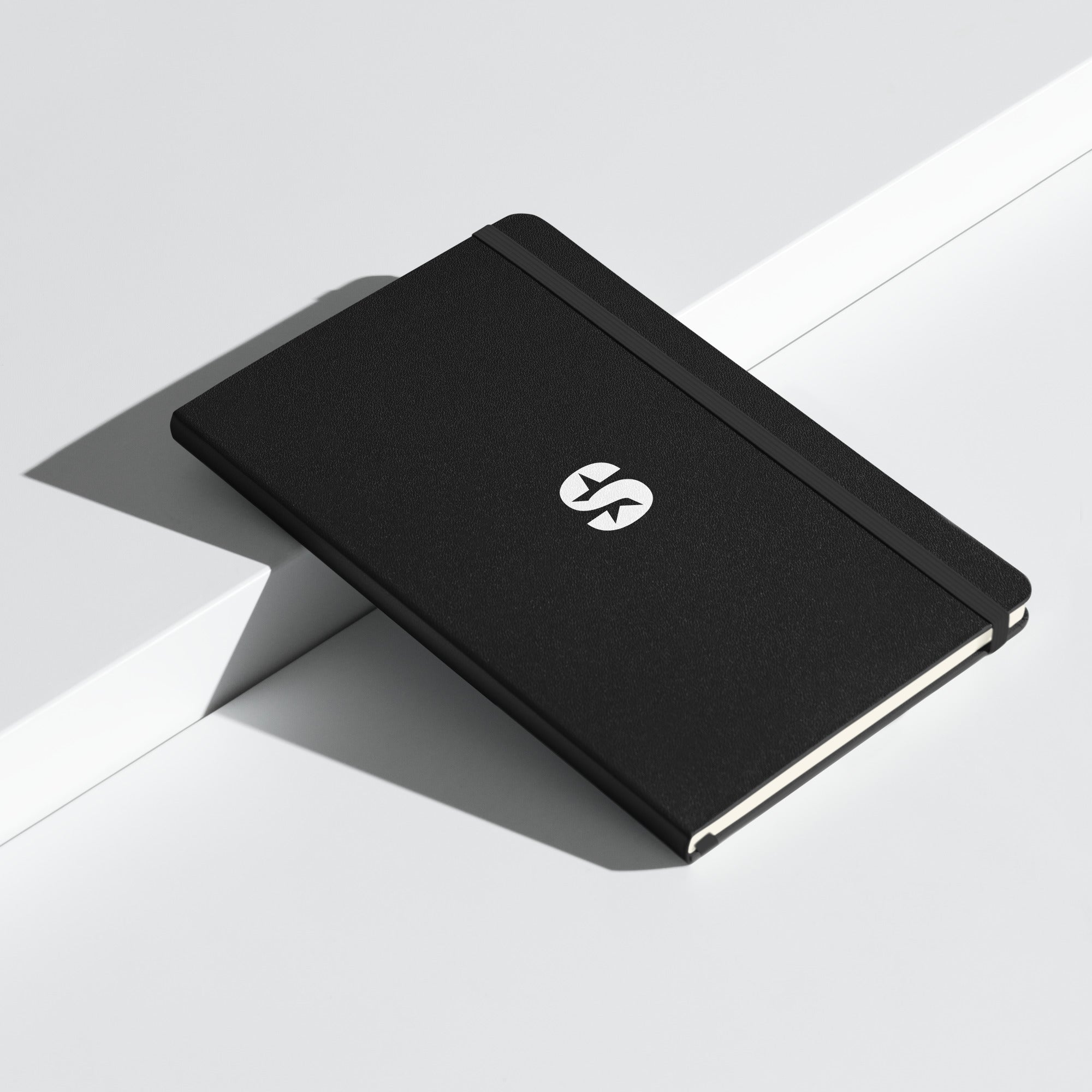 A black hardcover notebook with an elastic closure, featuring a minimalist 'SiriusXM' logo in white on the front cover. The notebook is placed on a modern, white surface with clean lines and shadows.