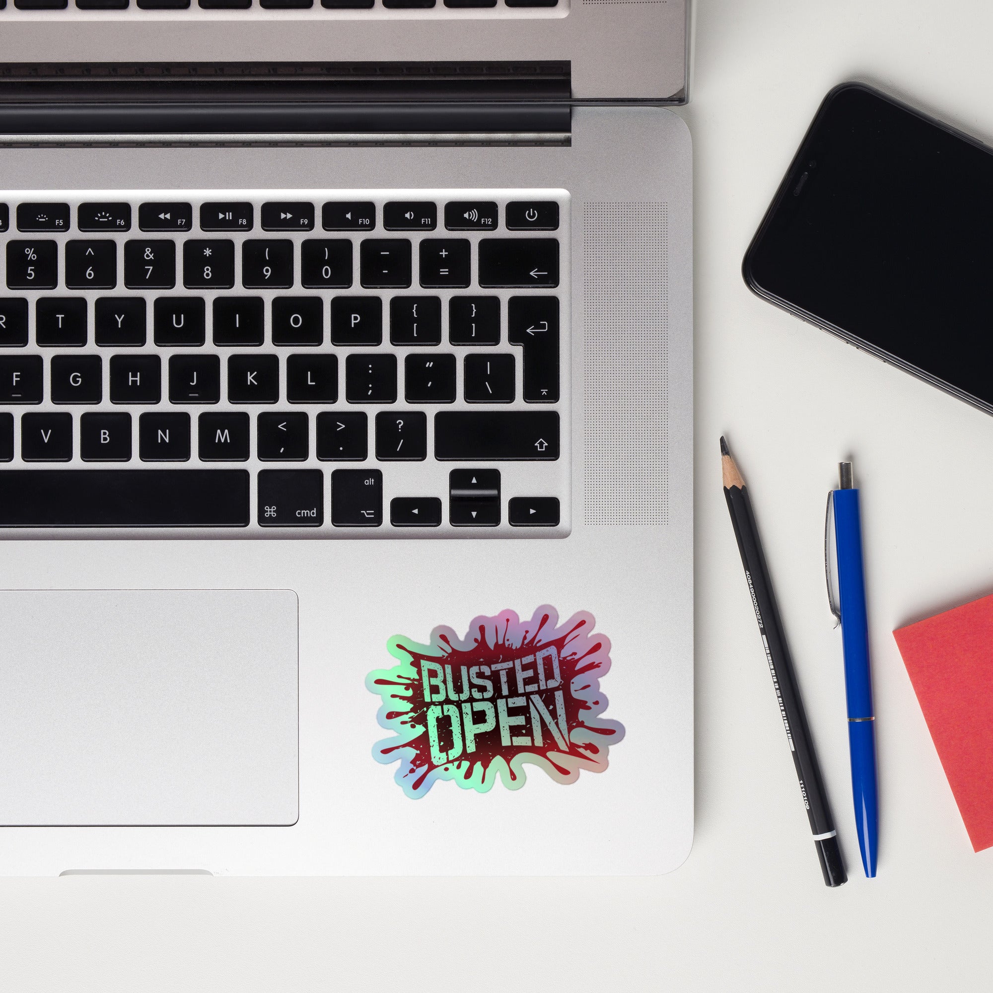 Close-up of a laptop keyboard displaying a colorful 'BUSTED OPEN' holographic sticker