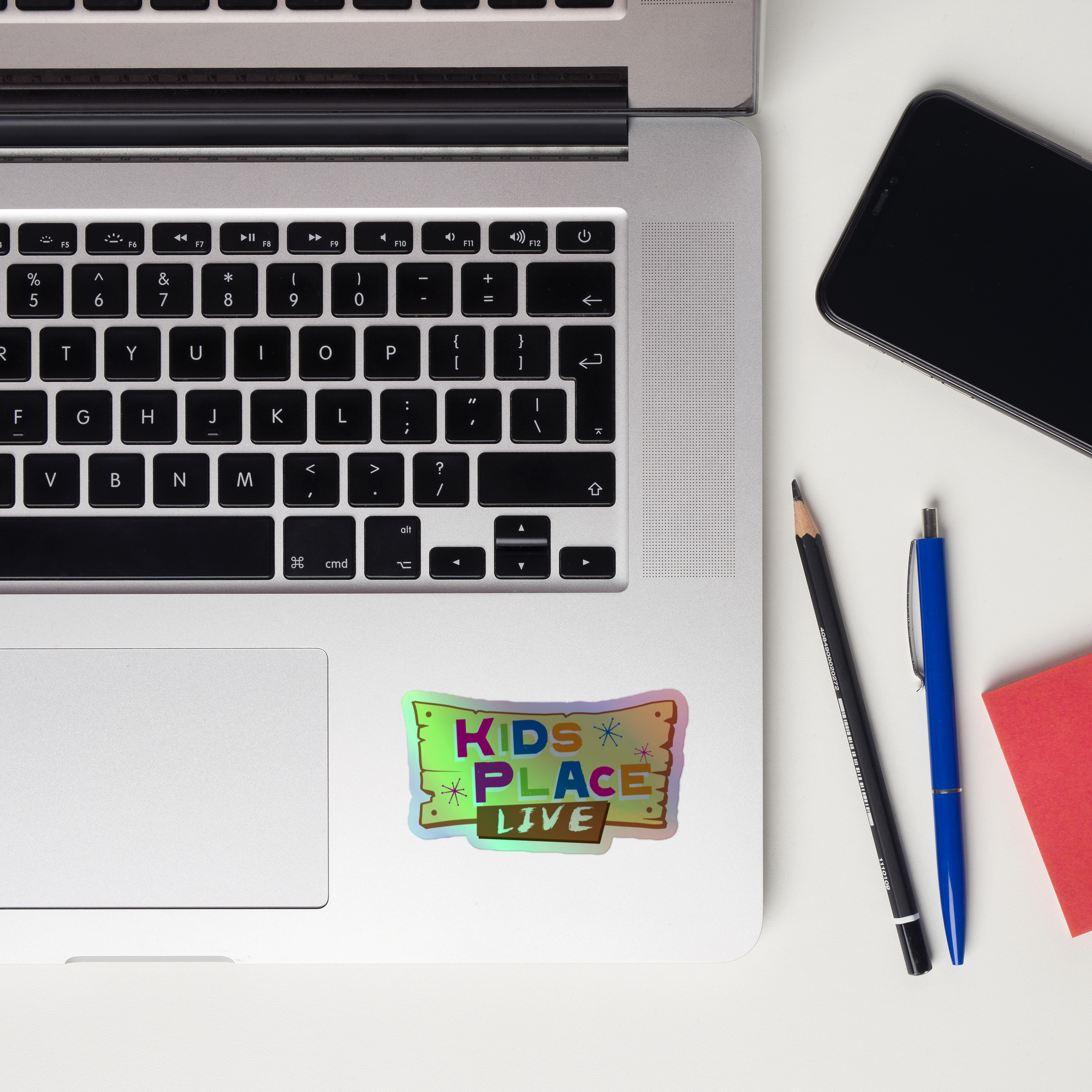 Laptop keyboard displaying colorful 'KIDS PLACE LIVE' holographic sticker.