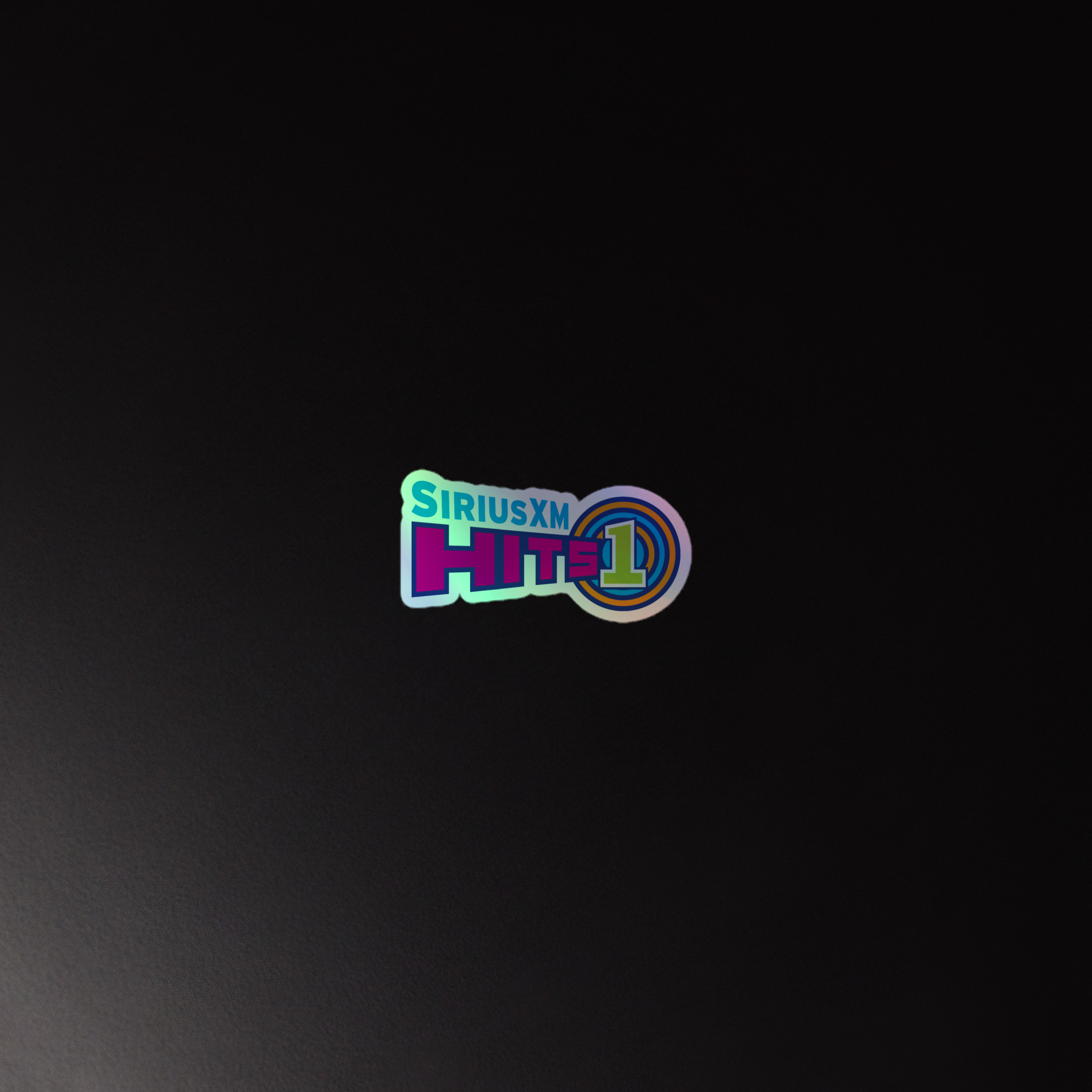 Holographic sticker of 'SiriusXM Hits 1' logo on a dark background, featuring colorful text and circular design elements.