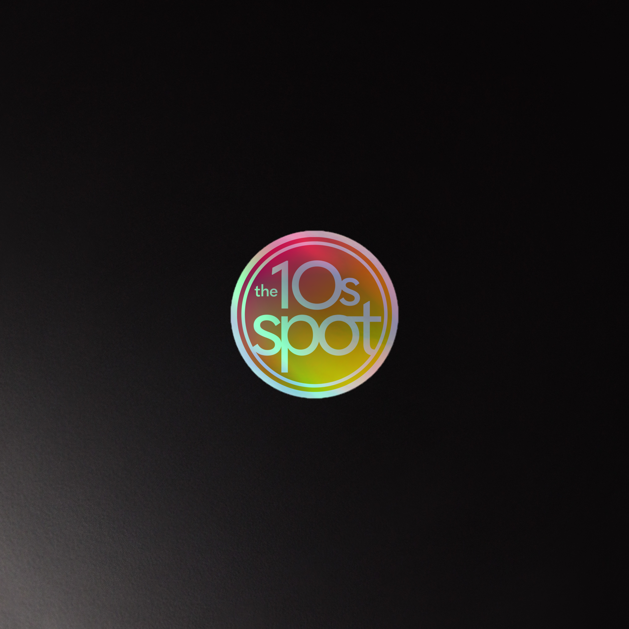 A holographic sticker of the circular 'the 10s spot' logo with a colorful gradient against a dark background.