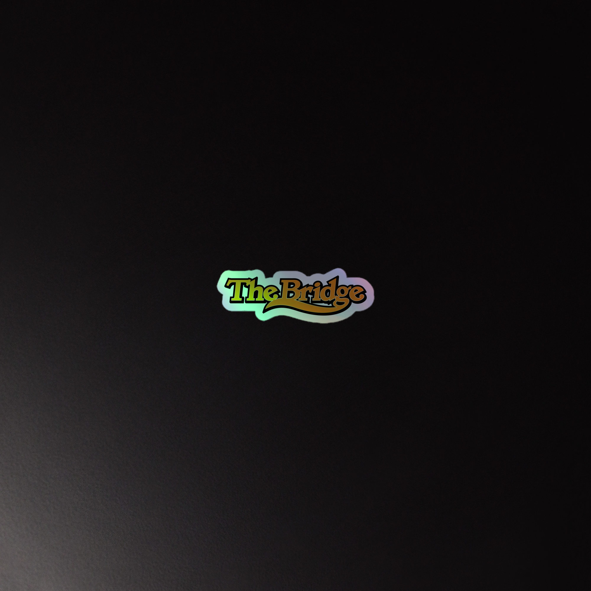 Colorful holographic sticker of the 'the bridge' logo on a dark background.