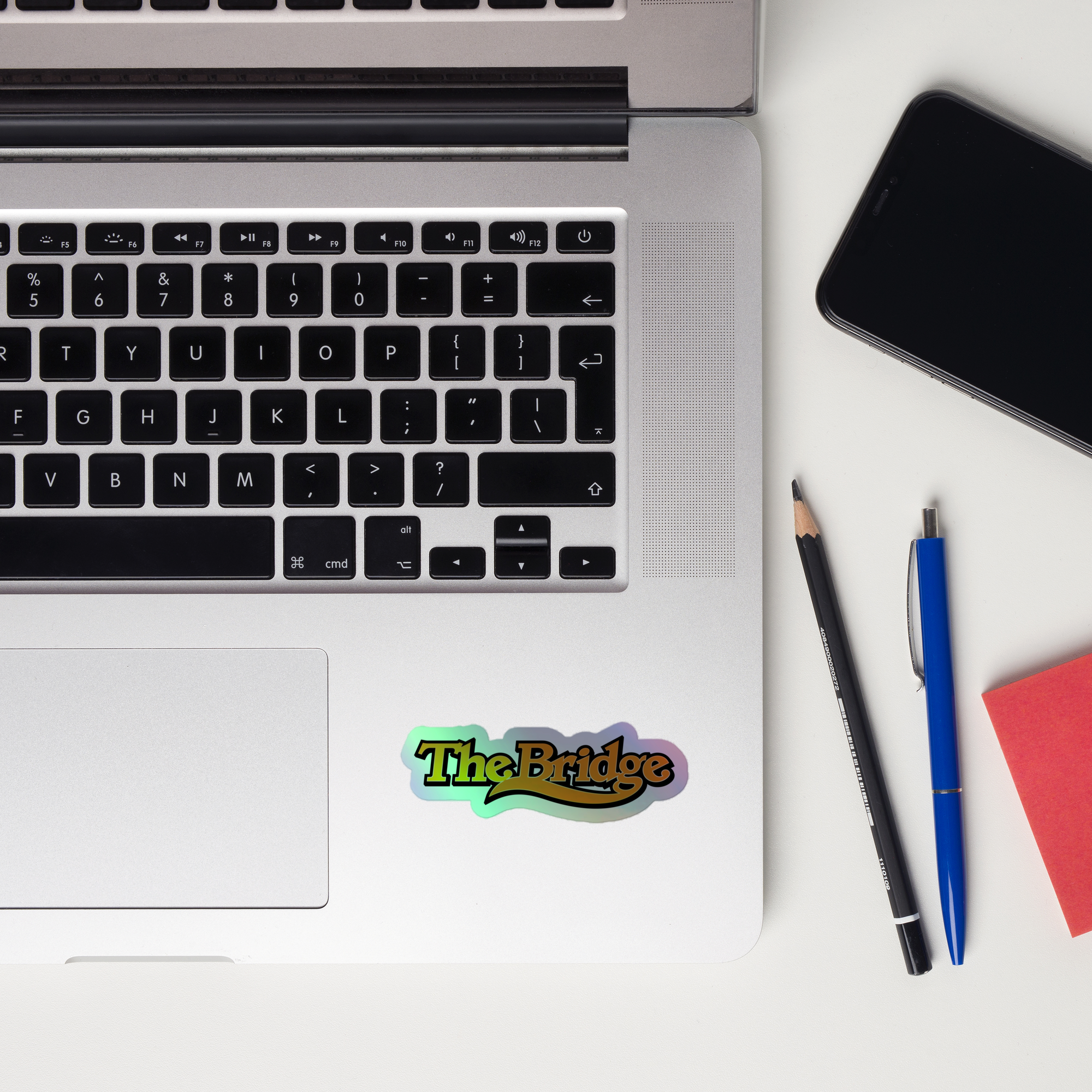 A laptop keyboard displaying a colorful 'The Bridge' holographic sticker.