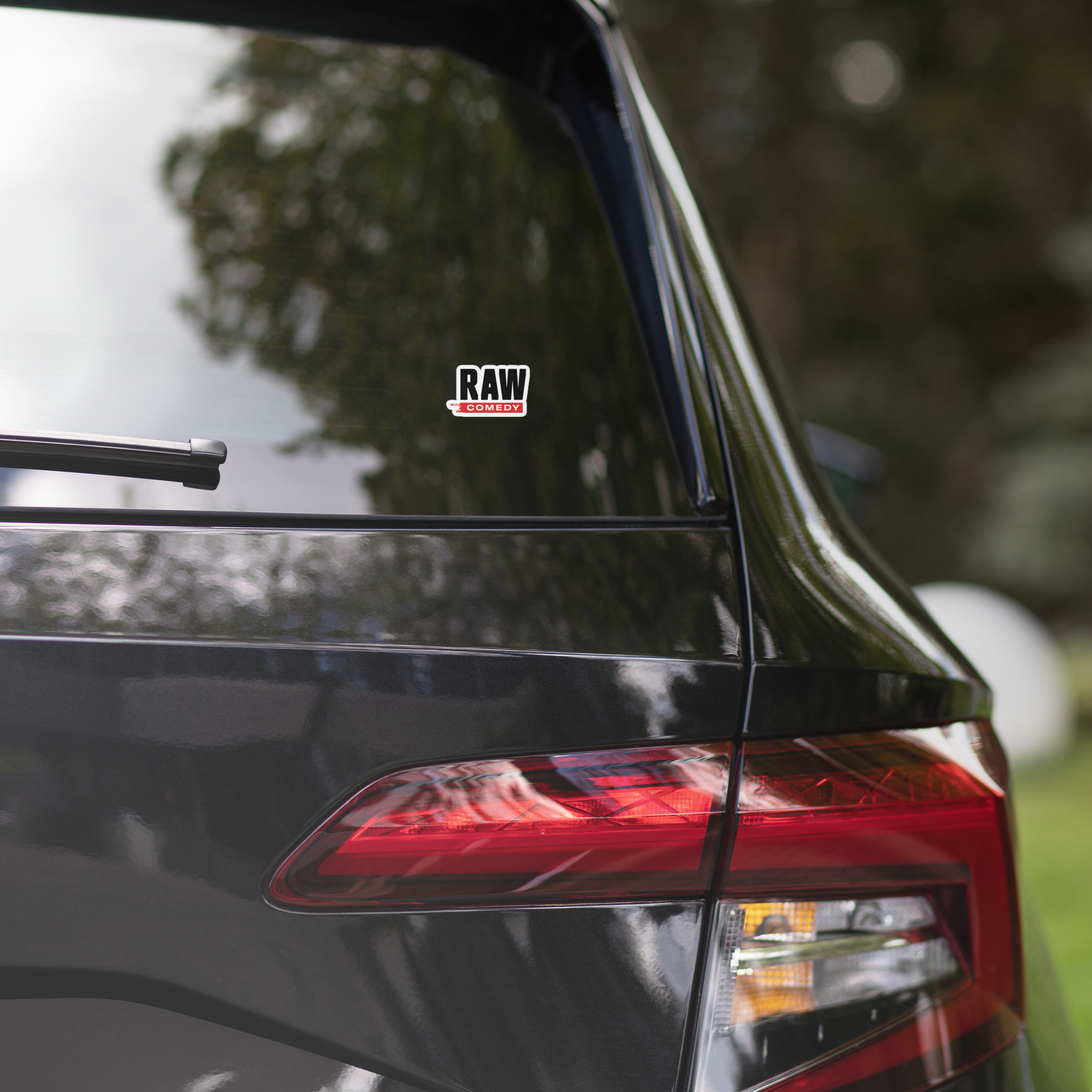 A black car's rear window features a 'Raw Comedy' sticker.