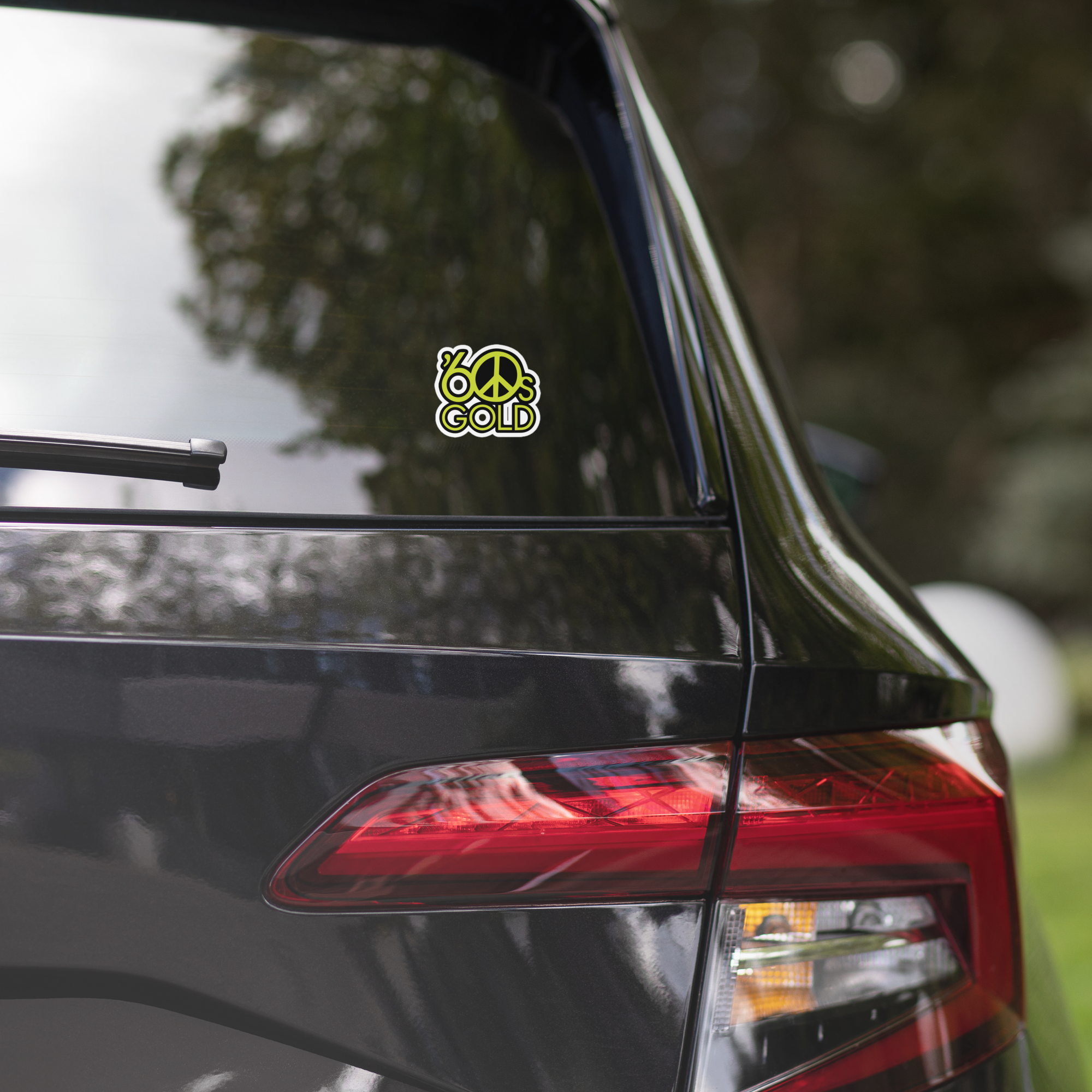 A black car's rear window displaying a colorful '60s Gold' peace sign sticker.