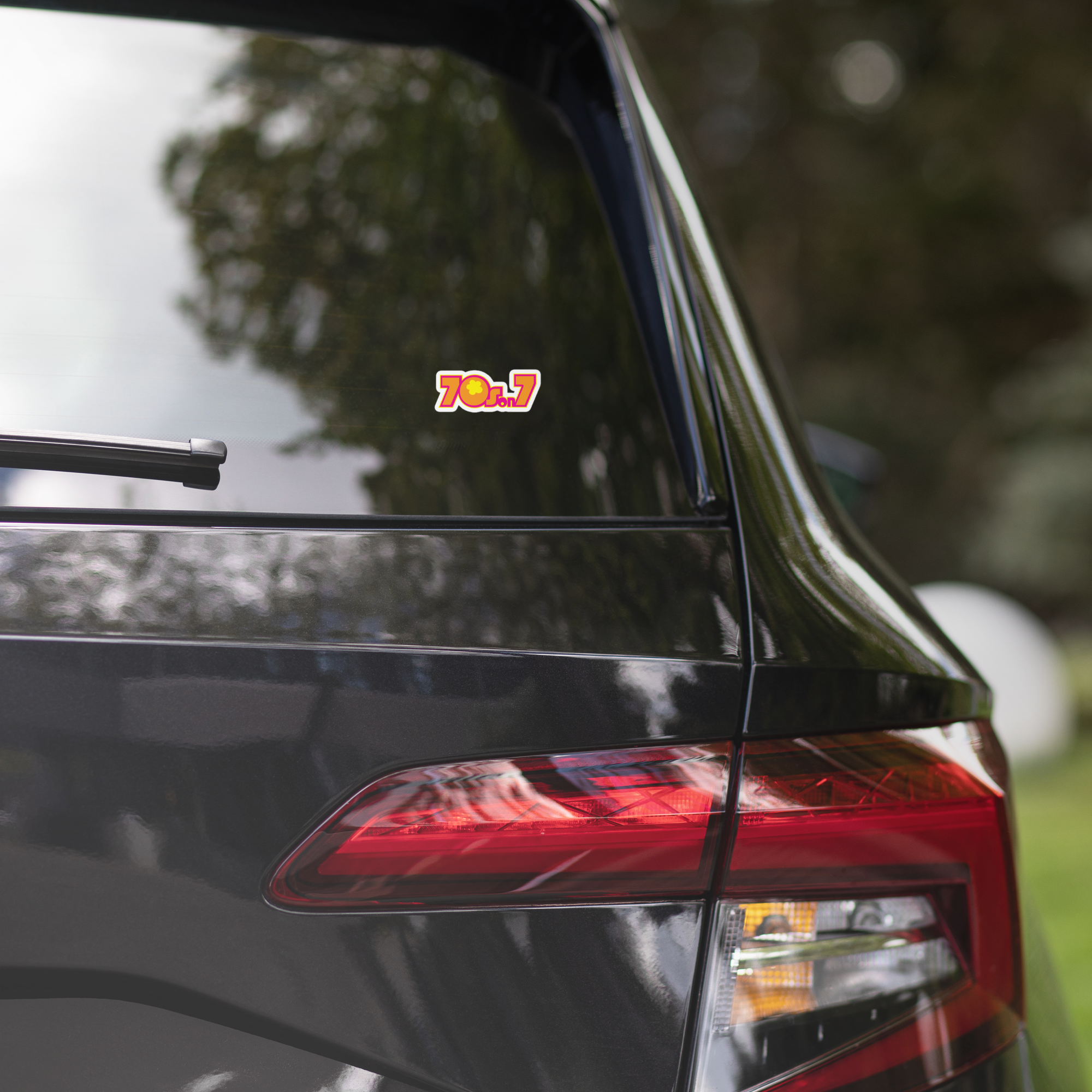 Close-up of a black vehicle's rear window displaying a colorful '70s on 7' sticker.