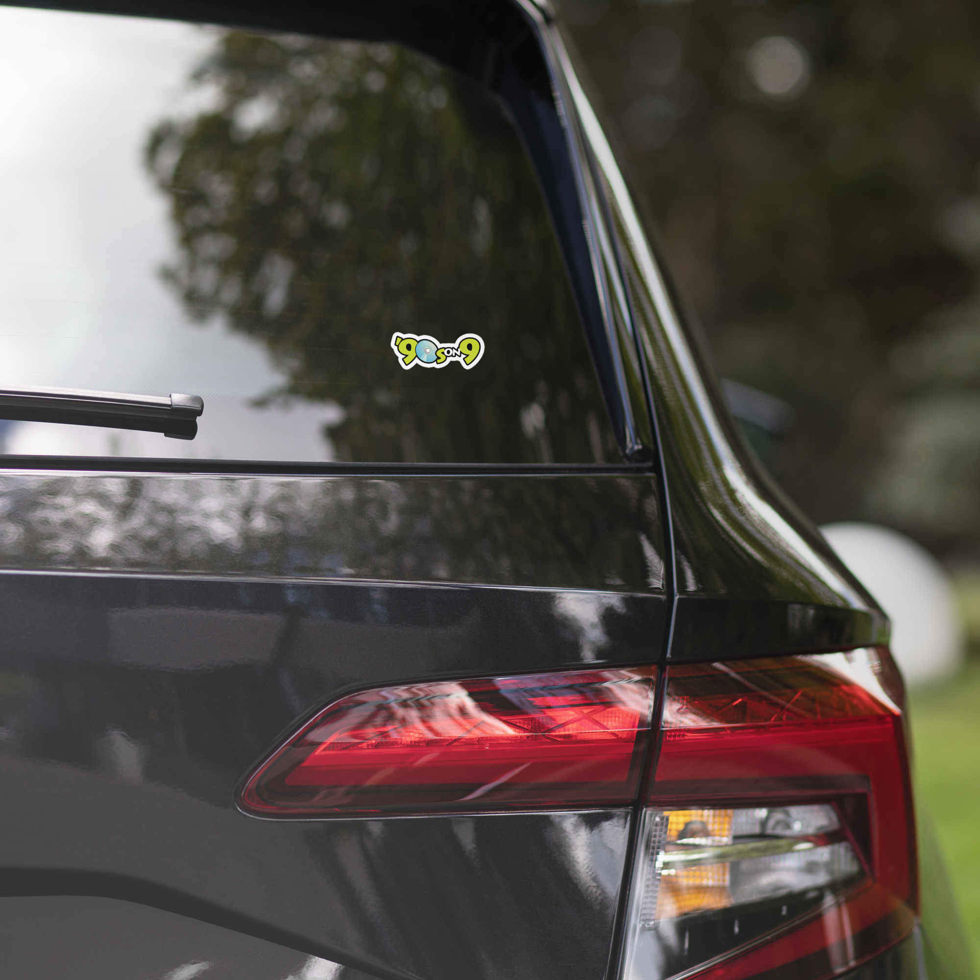 A black car's rear window features a '90s on 9' sticker.