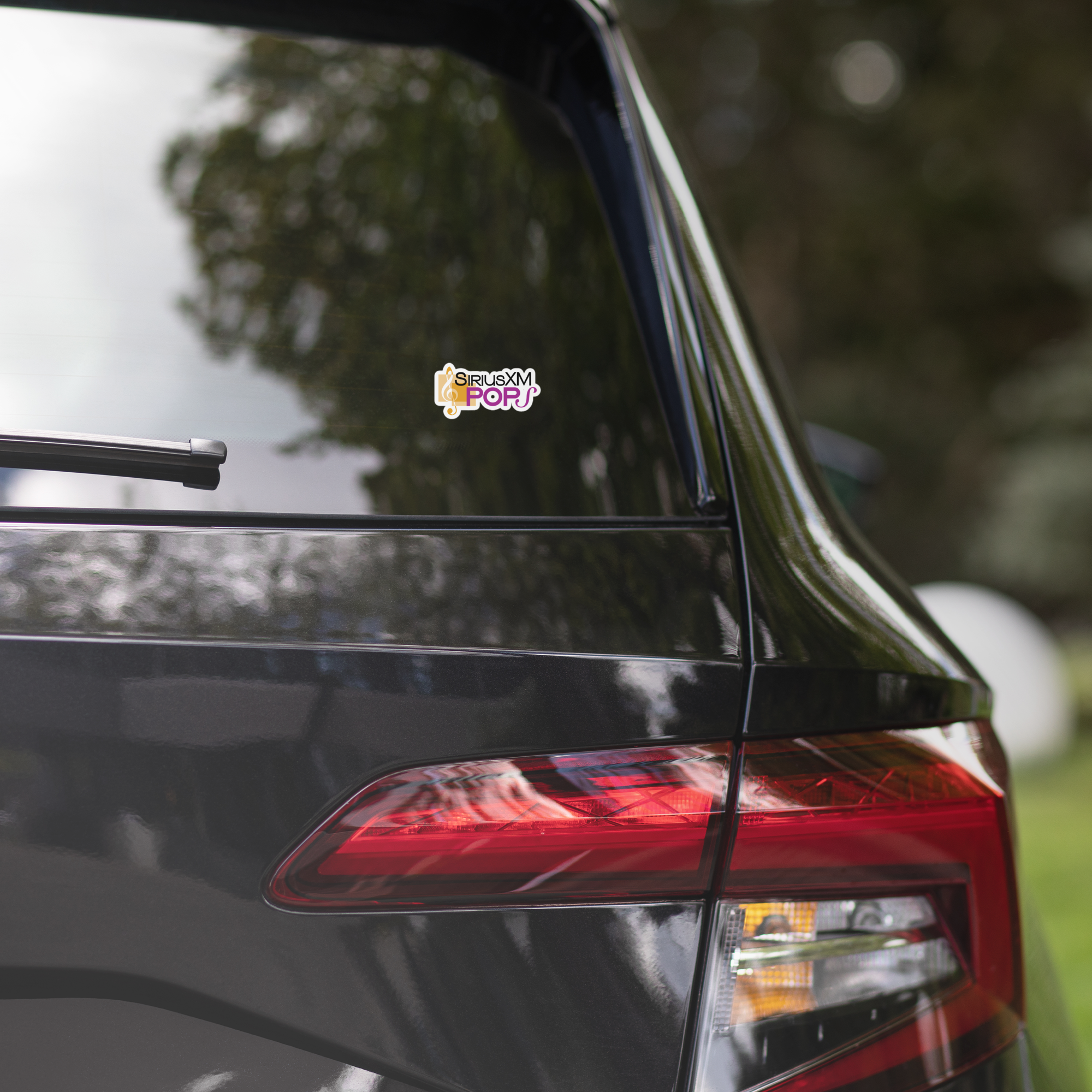 Close-up of a black car's rear with a 'SiriusXM Pops' sticker on the window.