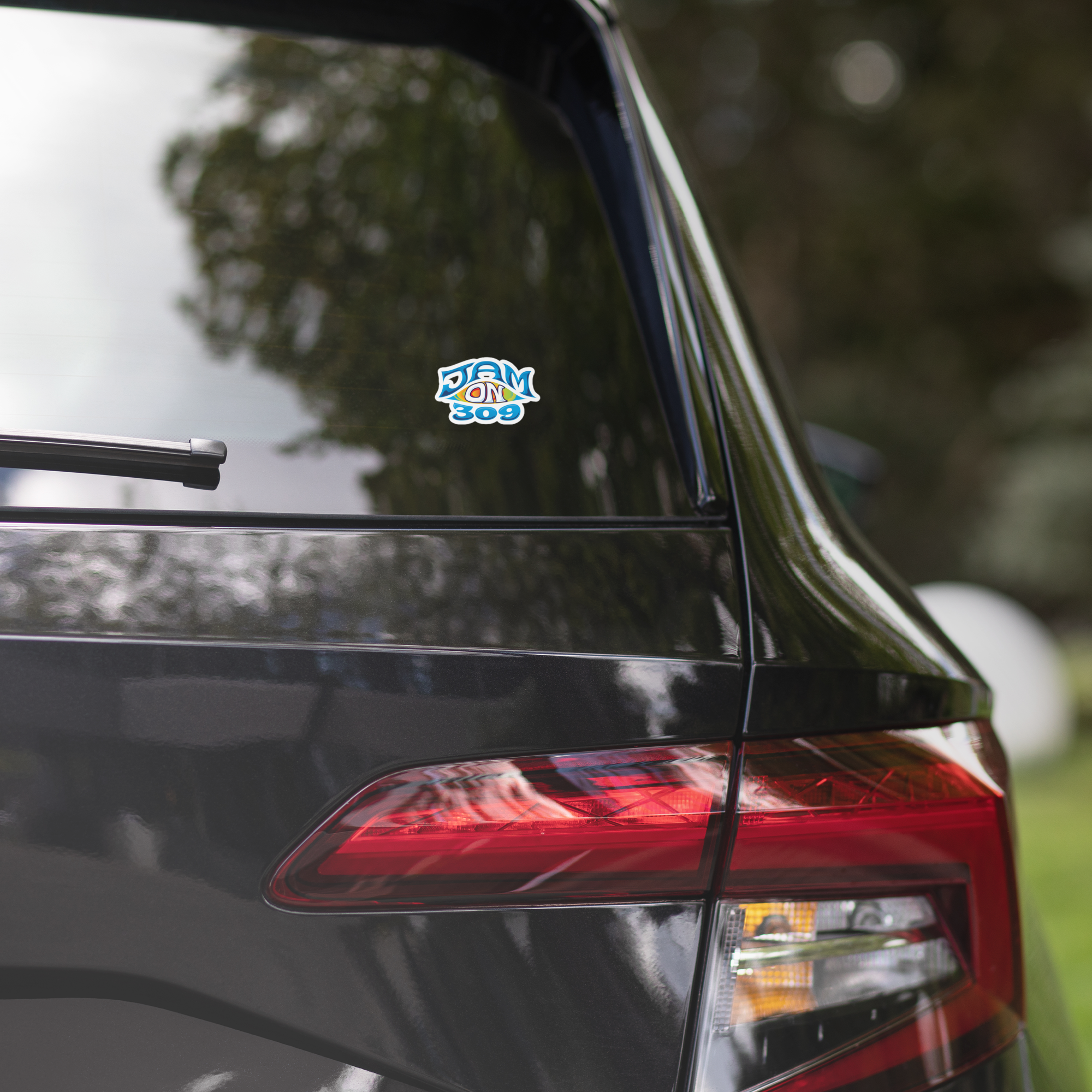 Close up of a black car's rear end displaying a 'Jam On 309' sticker on the back window.