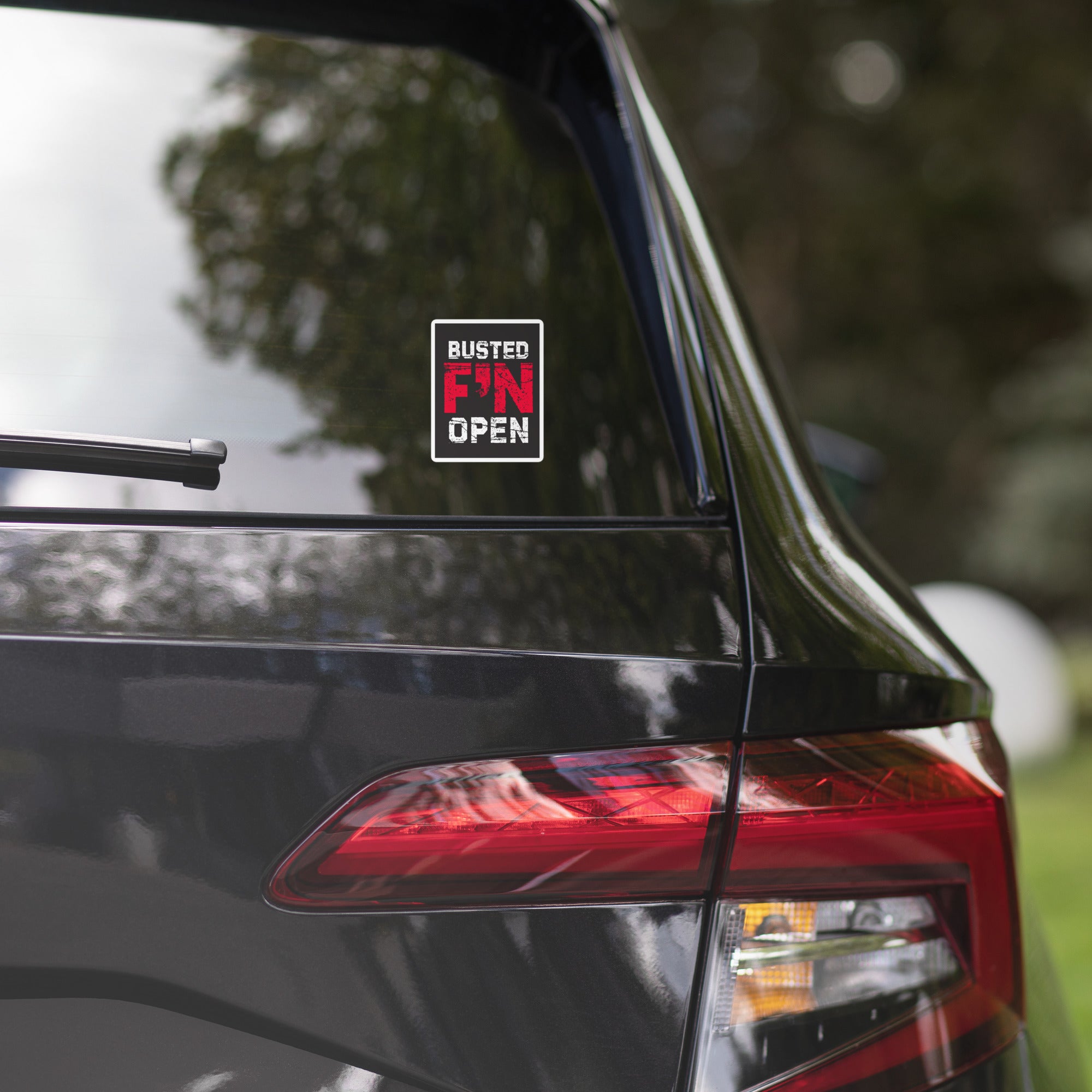 Car rear window featuring a sticker that says 'BUSTED F'N OPEN' in red, white and black.