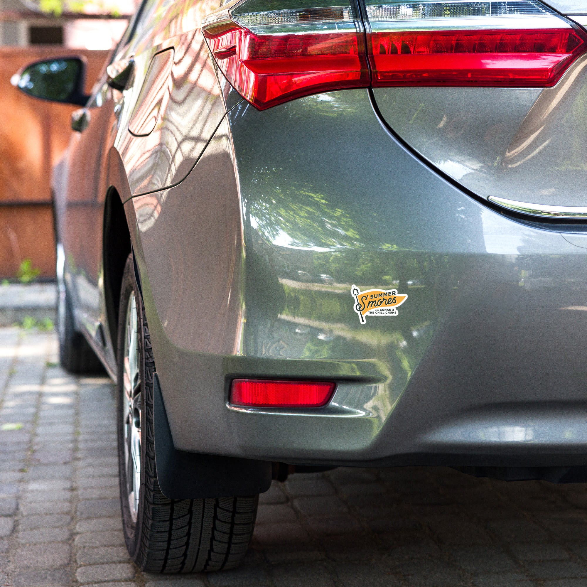 A close-up of the rear of a gray car, showing the taillight and a sticker that says 'SUMMER SMORES' near the bumper.