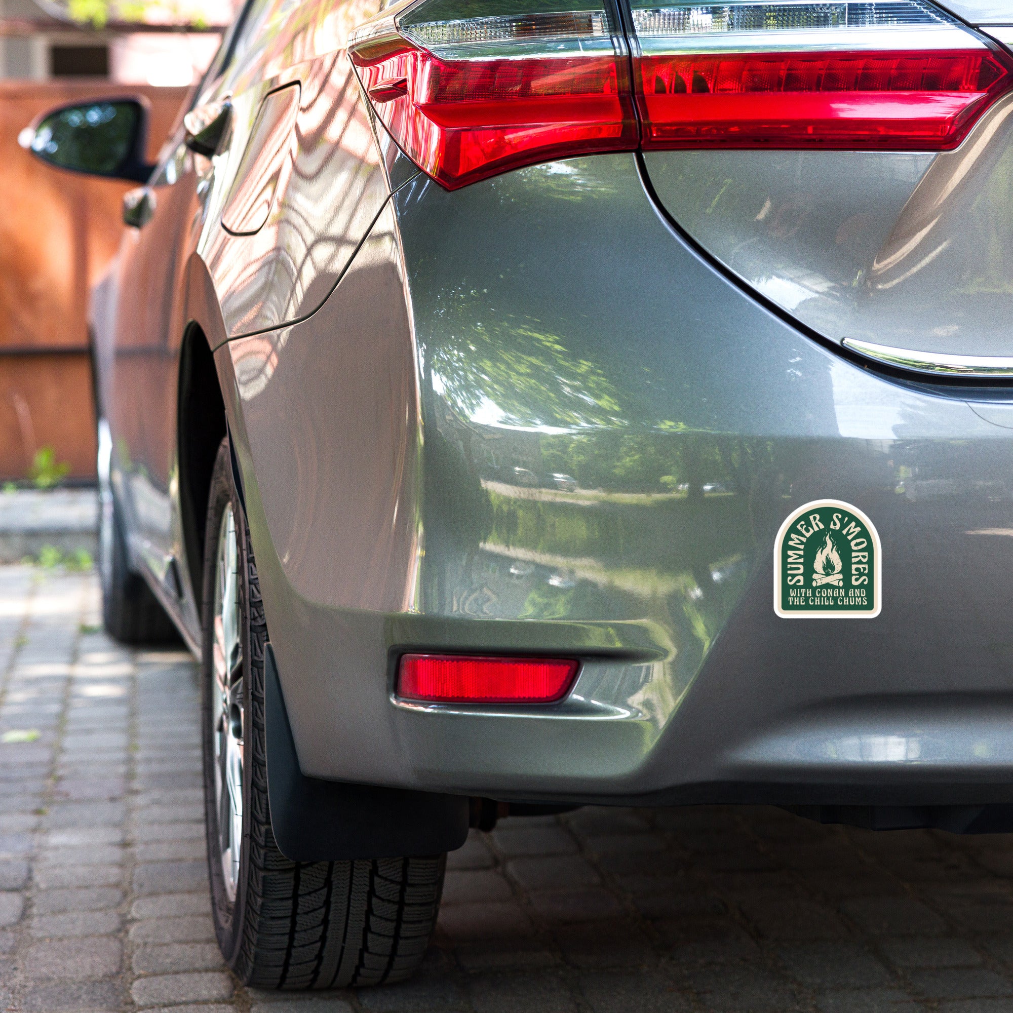 A view of the rear of a gray car, displaying the taillights and a sticker that reads 'Summer S'mores with Kona and the Chilo Kids.'