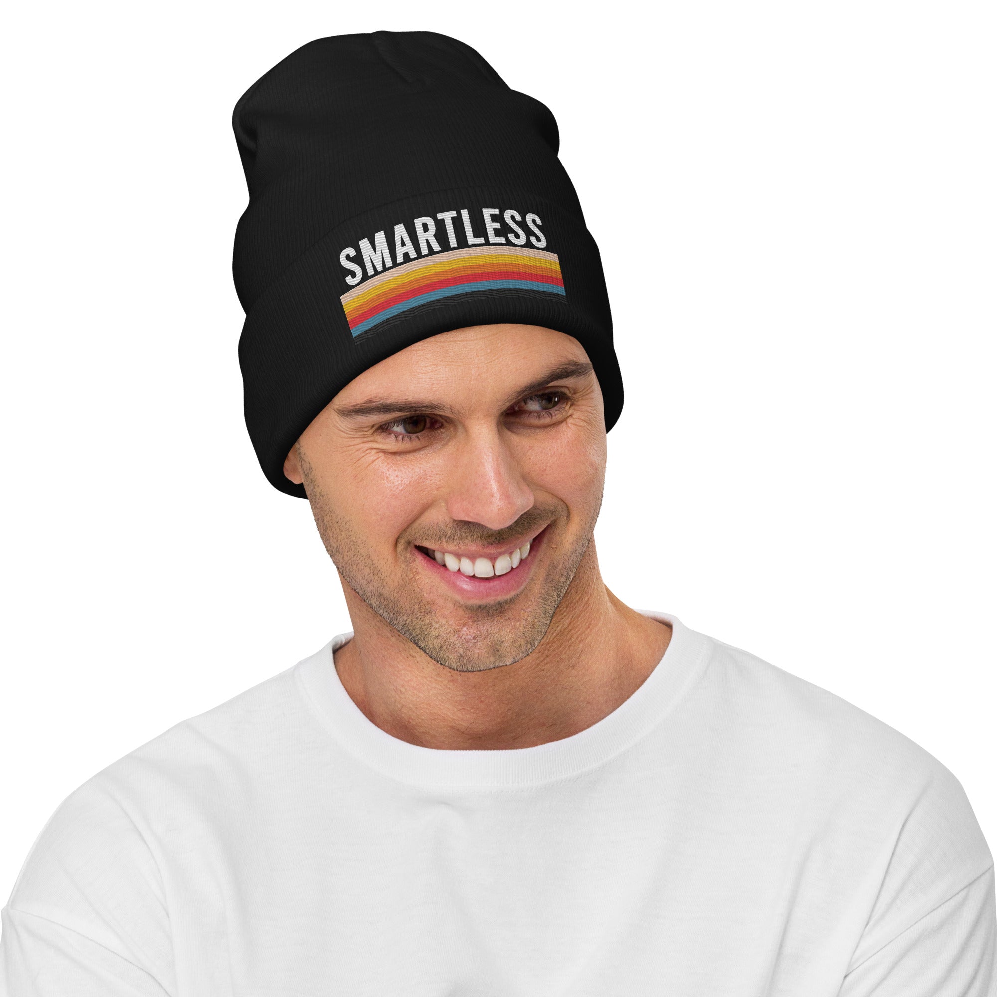 A smiling man wearing a black knit beanie featuring the word 'SMARTLESS' in bold white capital letters above a horizontal multicolored stripe pattern. The background is plain white.