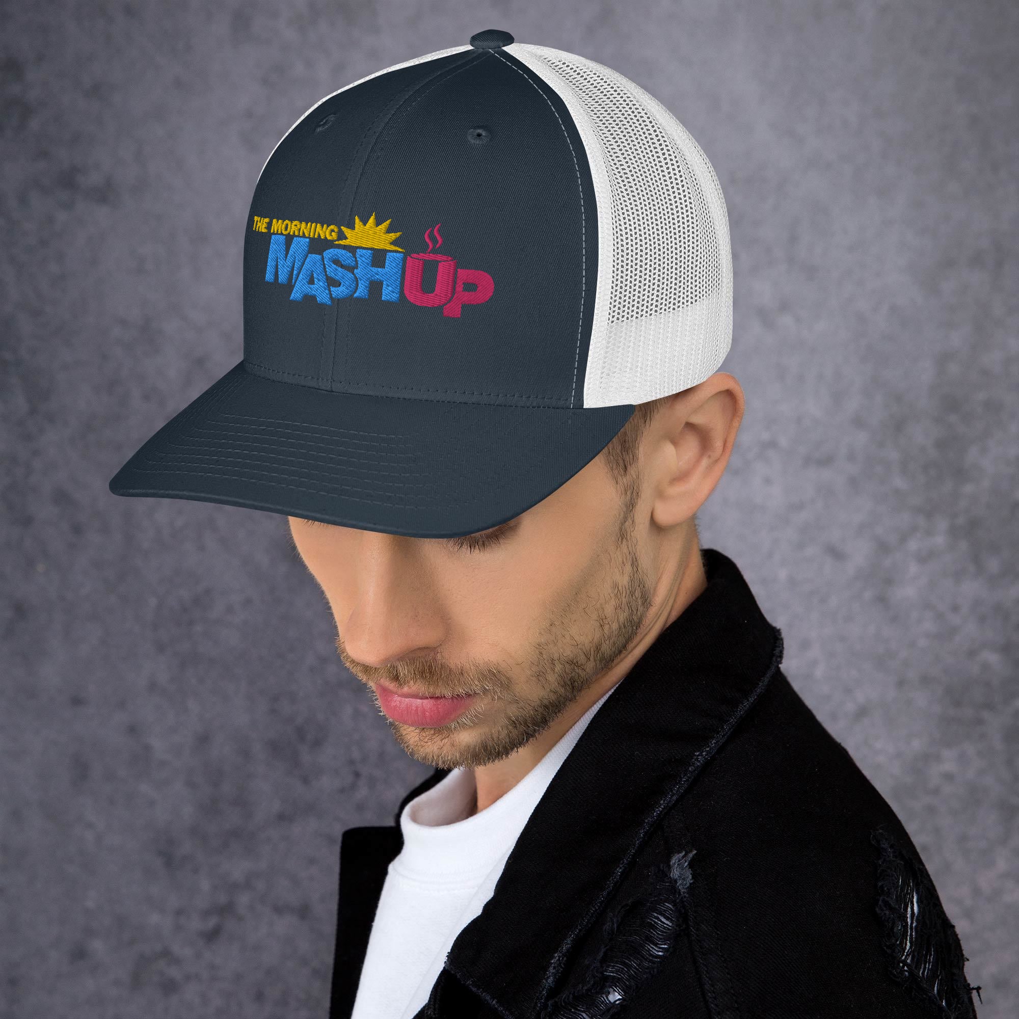 A black and white trucker hat featuring the logo 'THE MORNING MASH Up' with colorful blue, pink and yellow text including a sun and a coffee cup.