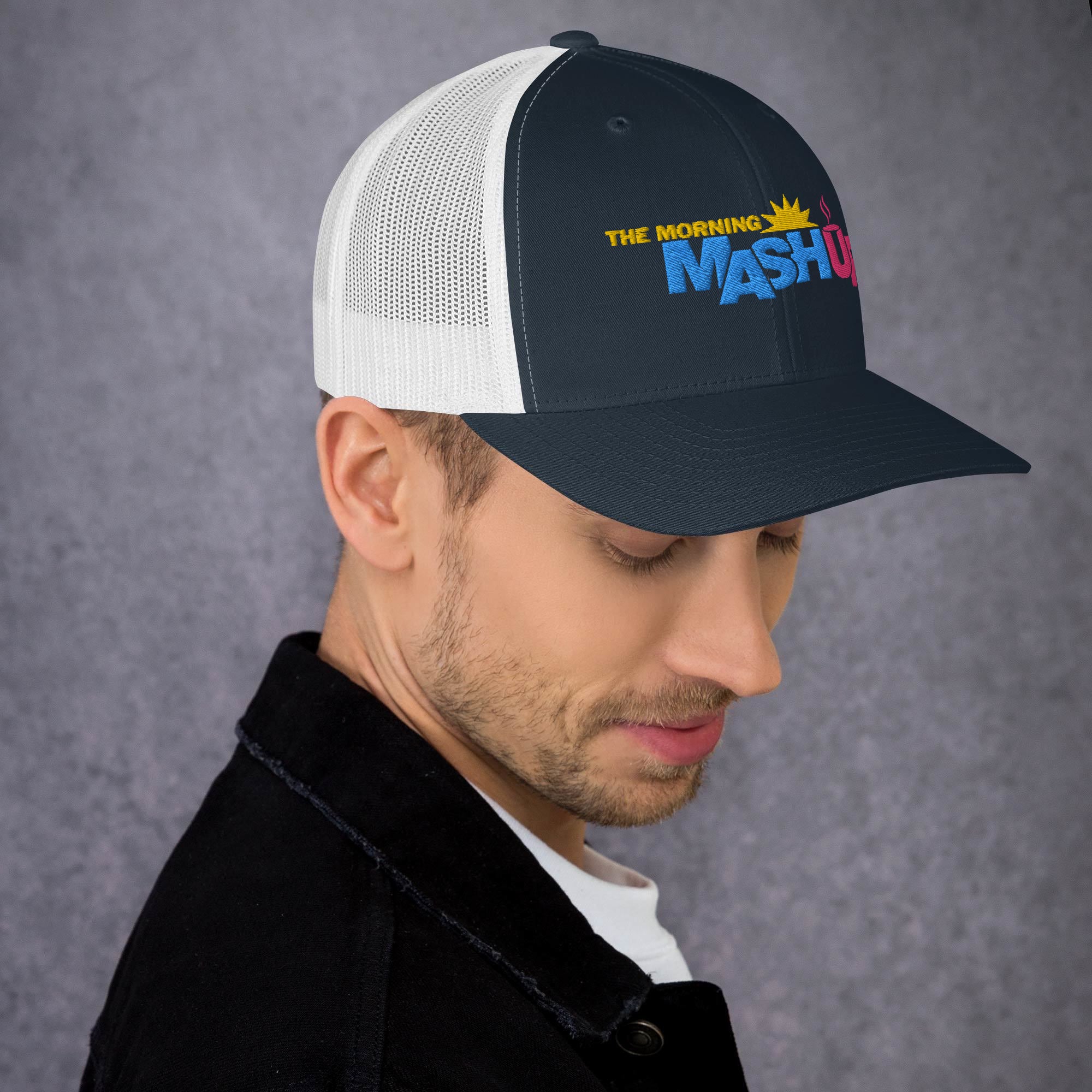 A black and white trucker hat featuring the logo 'THE MORNING MASH Up' with colorful blue, pink and yellow text including a sun and a coffee cup.