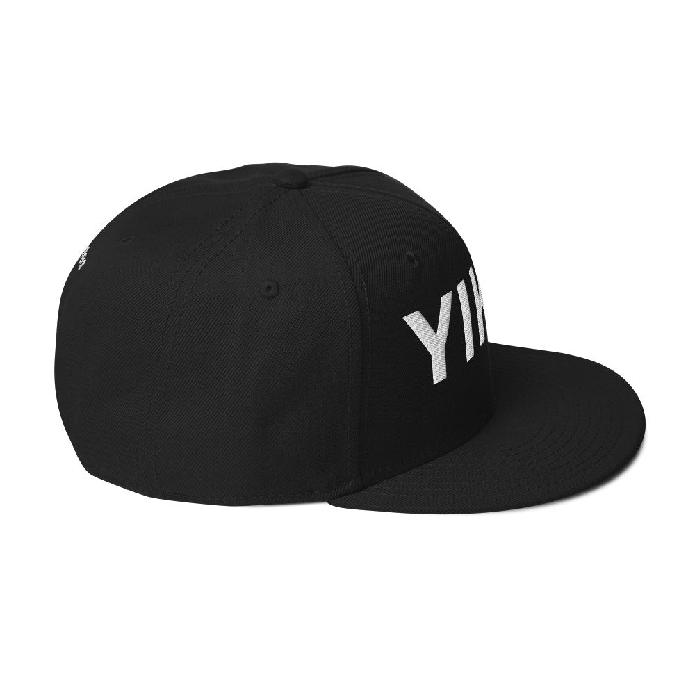 Side view of black hat with light grey letters on front.