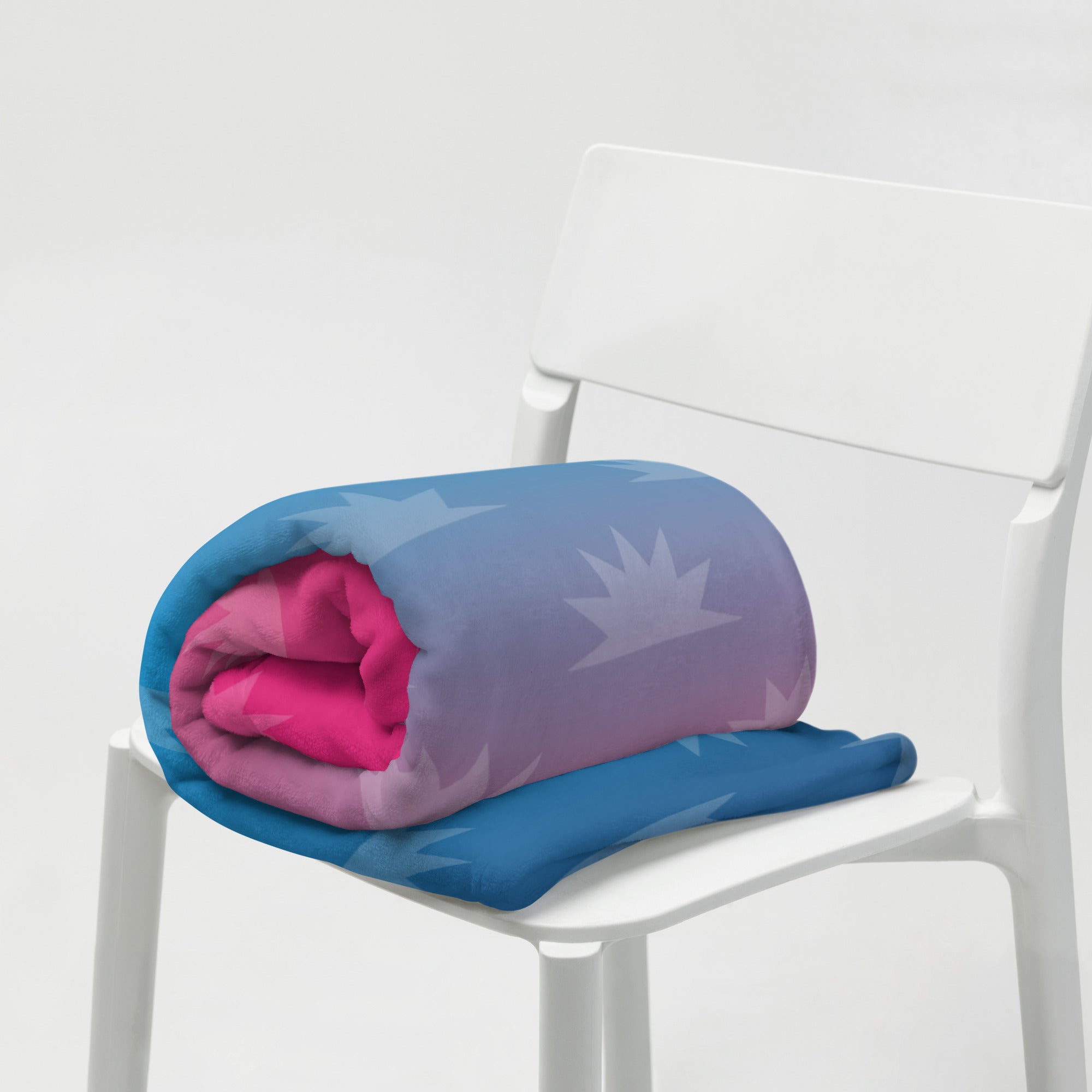 A rolled blanket with a blue and pink gradient design with star patterns placed on a white chair.