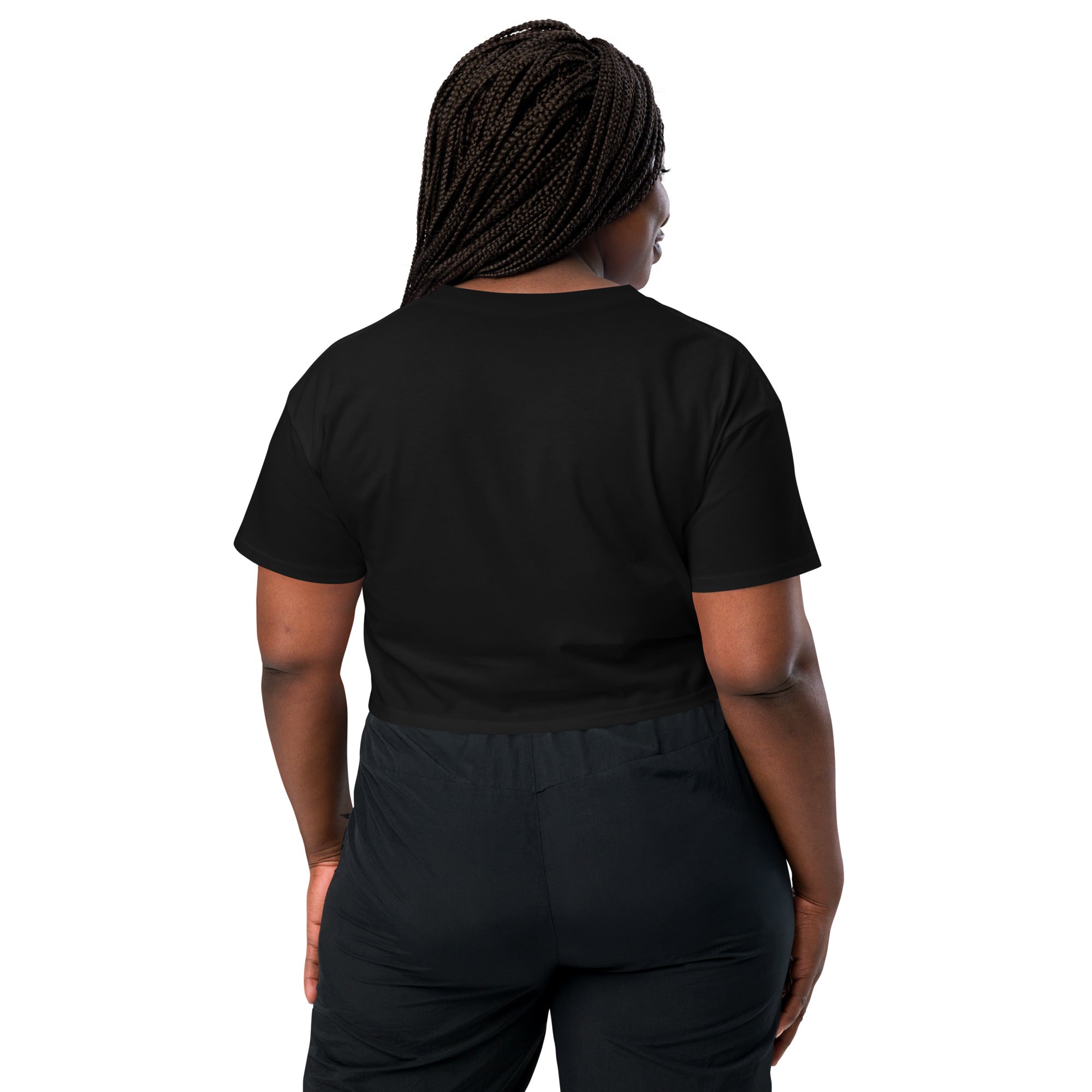 The back view of a woman wearing the black crop top. The clean design of the t-shirt is stylish and the cut is flattering. She is wearing black high-waisted pants and has long braided hair.