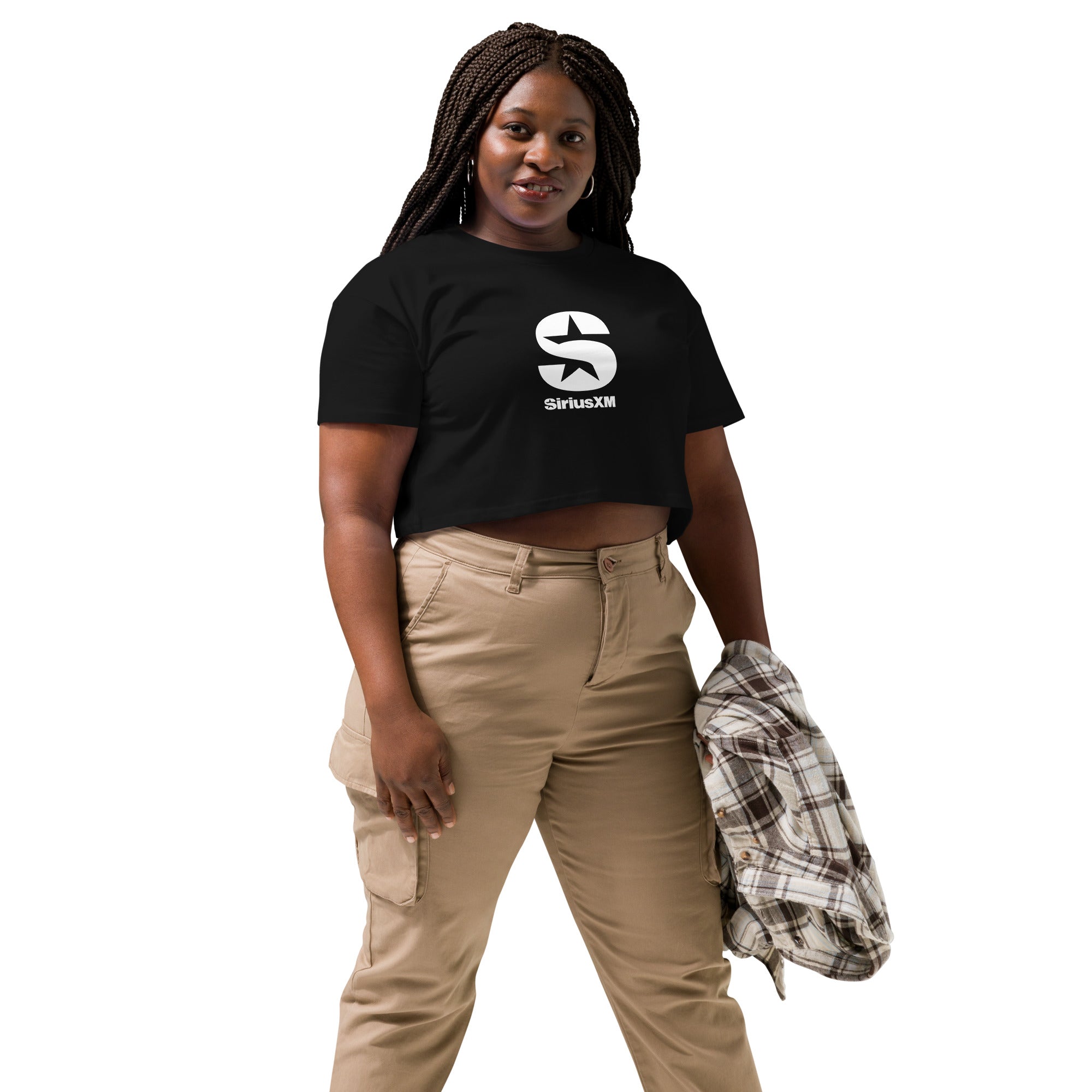 A woman wearing a black 'SiriusXM' crop top with a bold white logo on the chest. She pairs it with beige cargo pants and holds a plaid jacket in her hand, posing confidently.