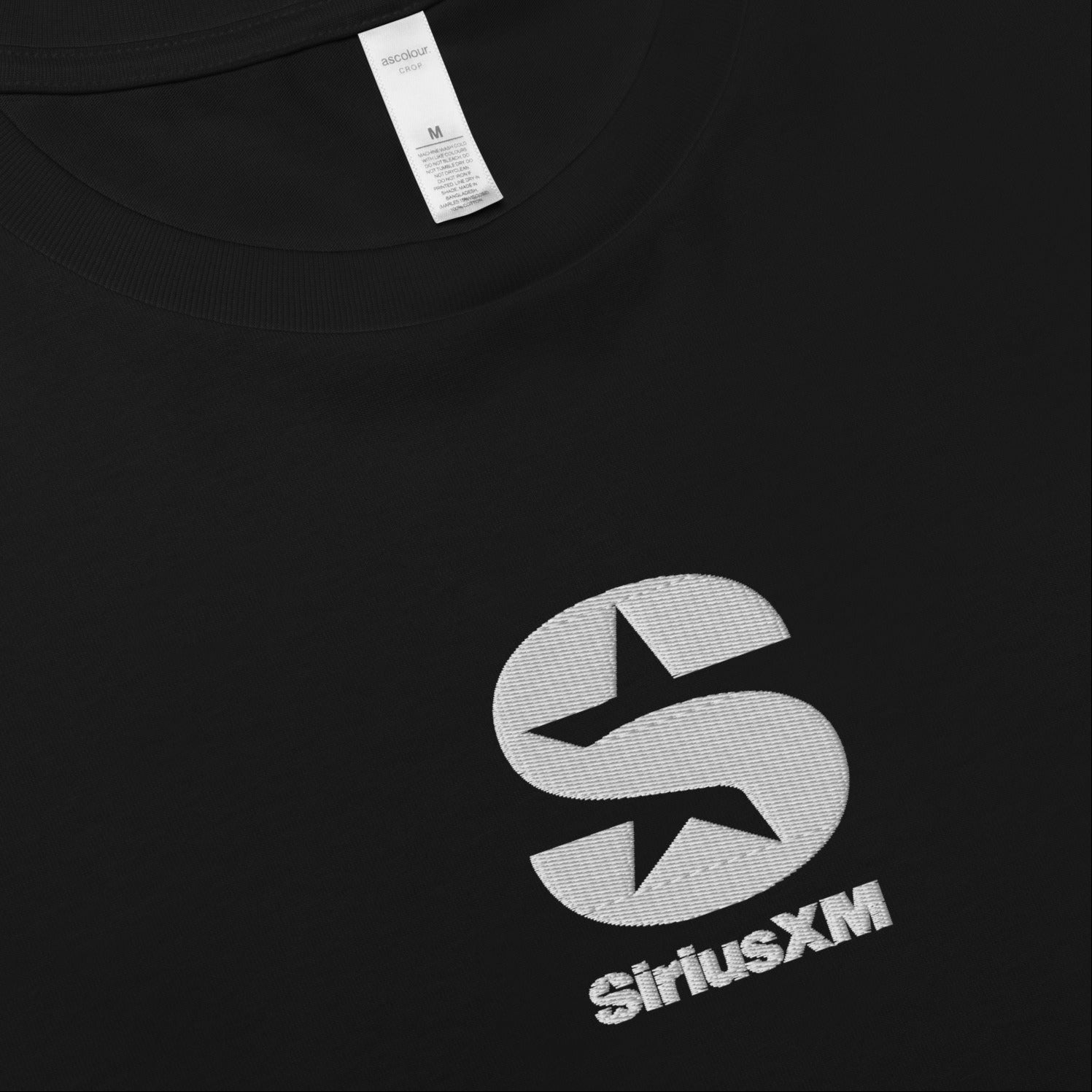 A close up, flat-lay shot of the black crop T-shirt, highlighting the 'SiriusXM' logo's high-quality embroidery with shiny white  thread on the chest.